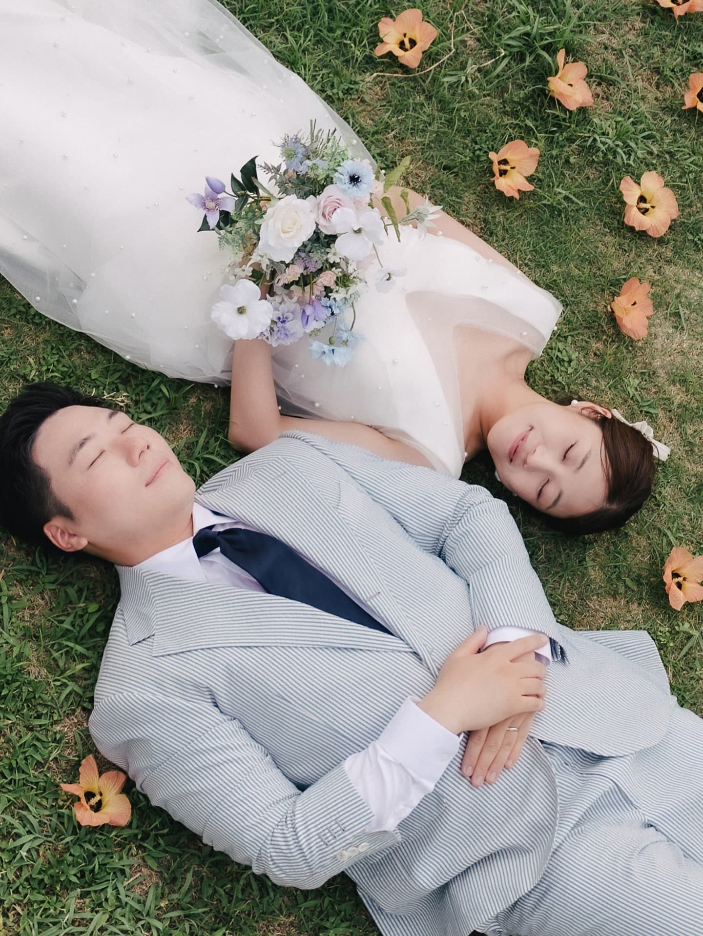꽃잎 흩어진 잔디밭에 나란히 누운 신랑신부, 오키나와 야외 촬영