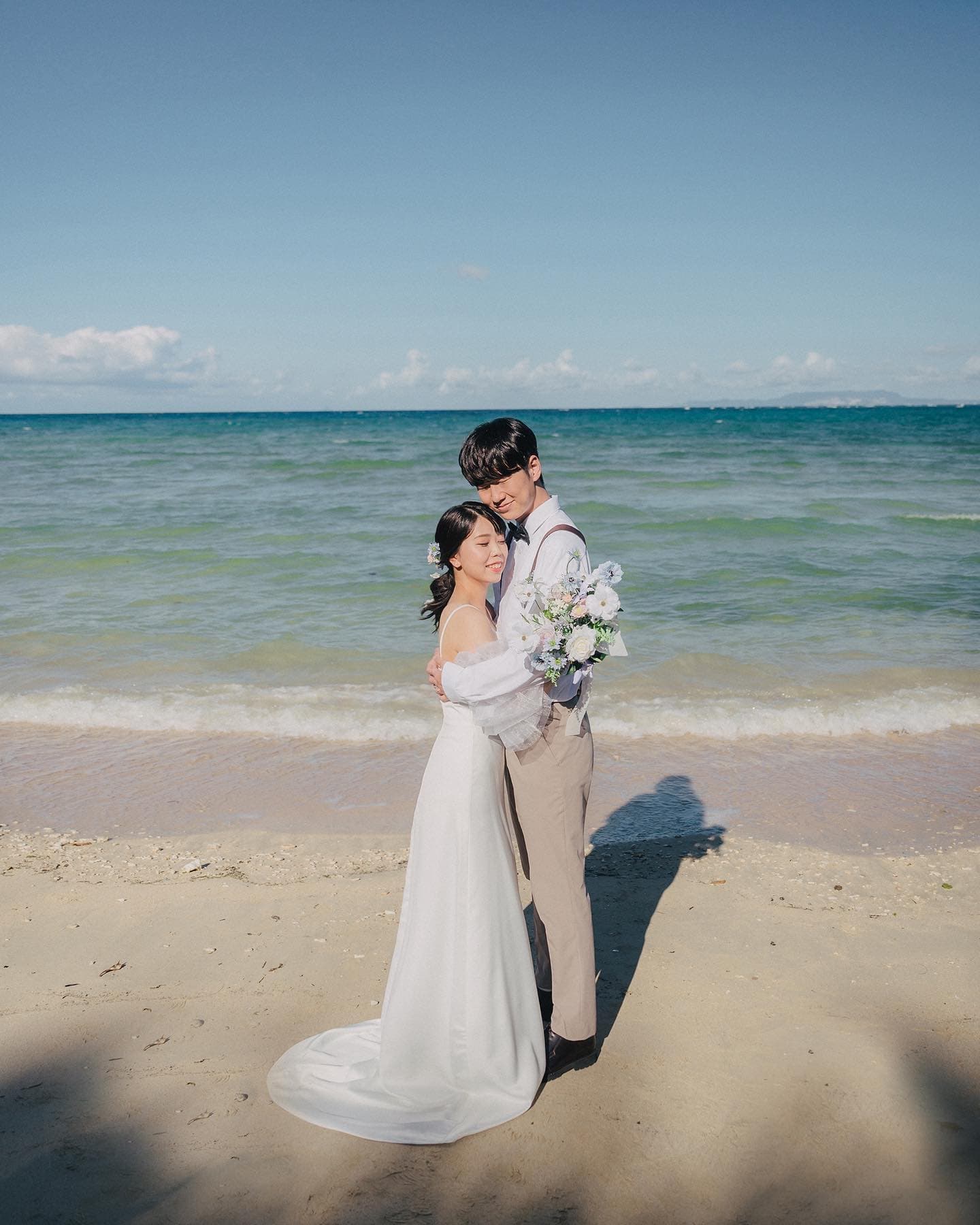エメラルドの海辺でブーケを持って抱き合う新郎新婦、沖縄