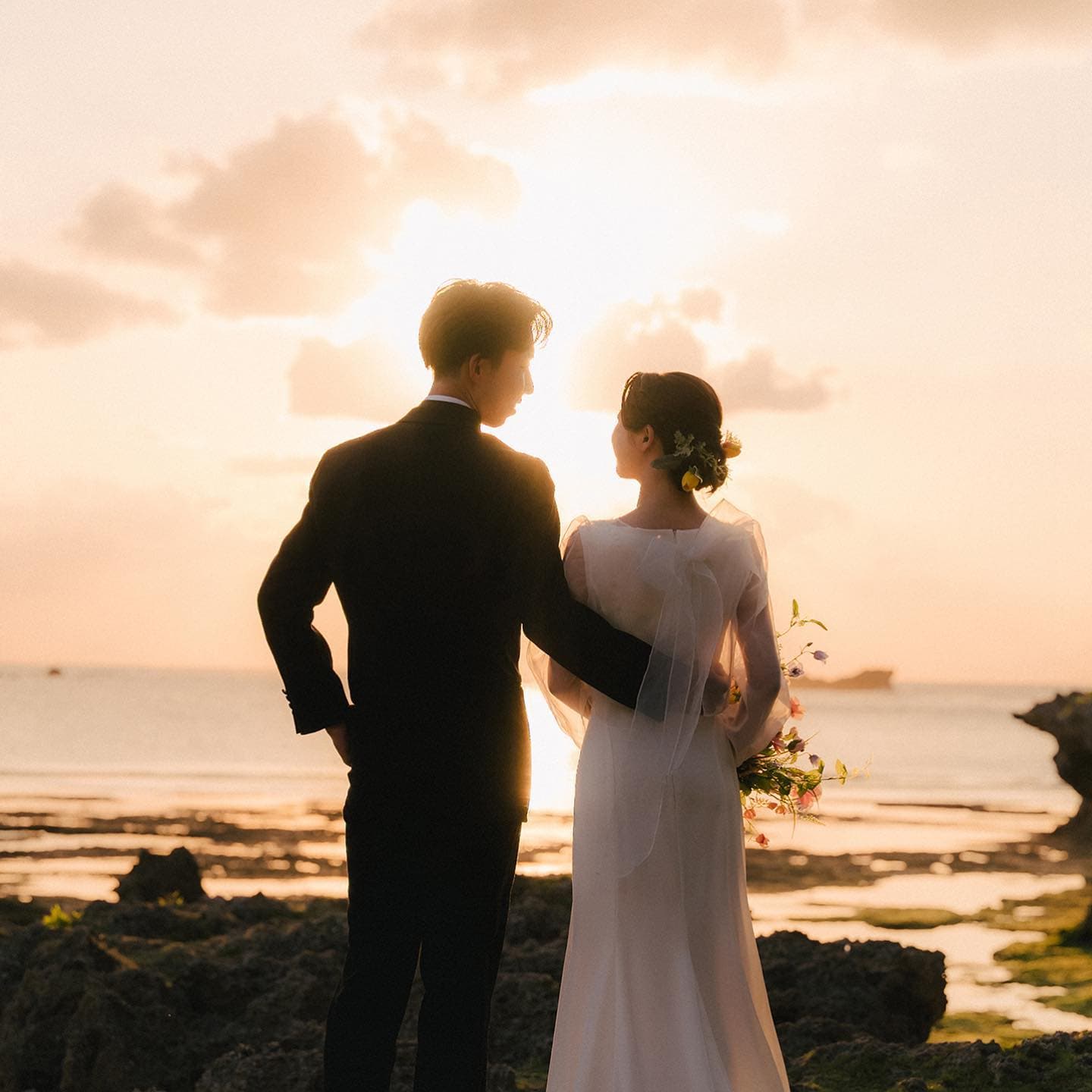 Couple seen from behind watching the sun set over the sea from a rocky Okinawa shore