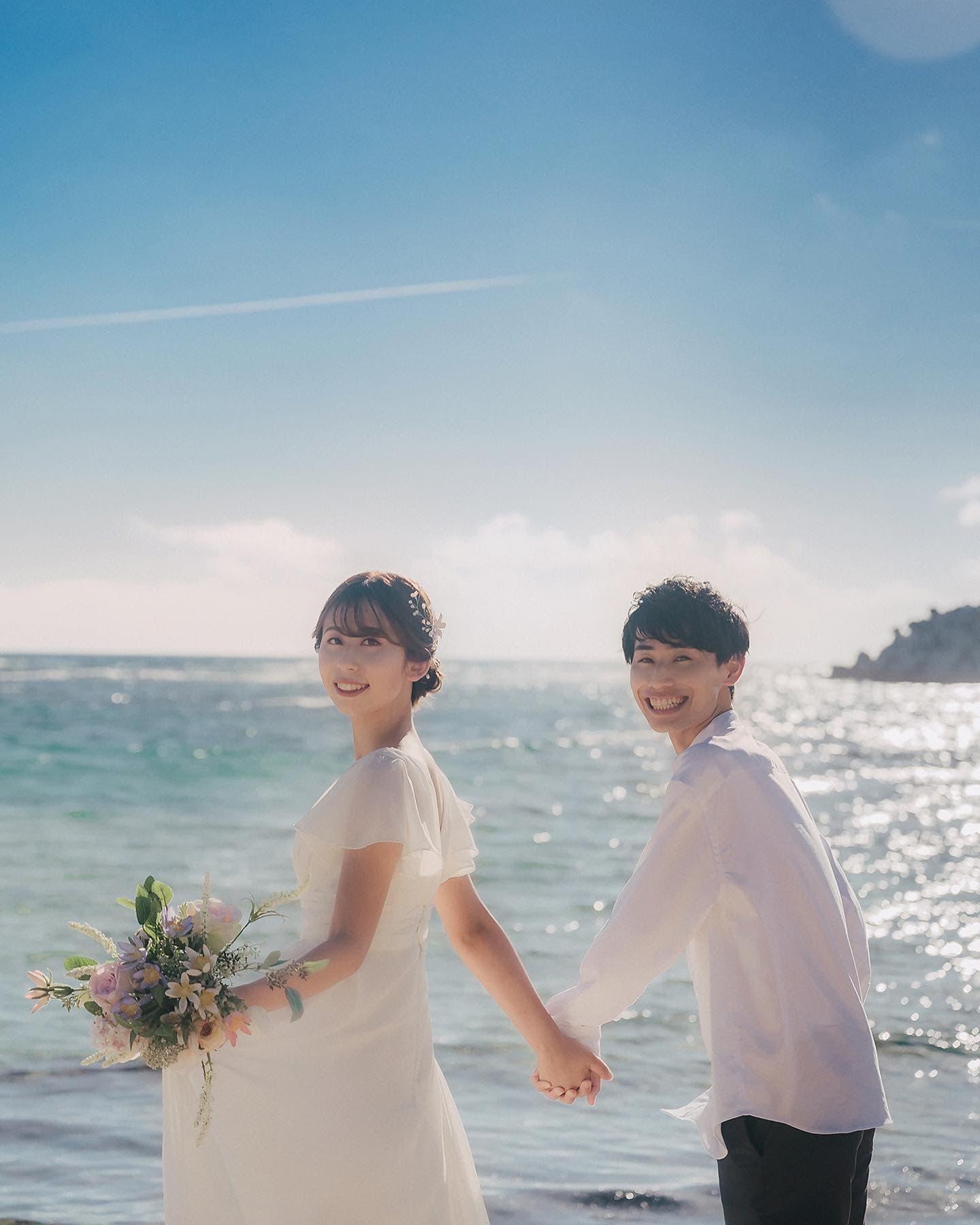 Couple holding hands and looking back over a bright blue sea in Okinawa