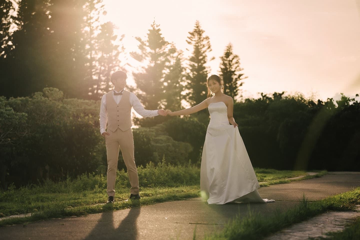 Groom reaching for his bride's hand on a backlit path at dusk in Okinawa