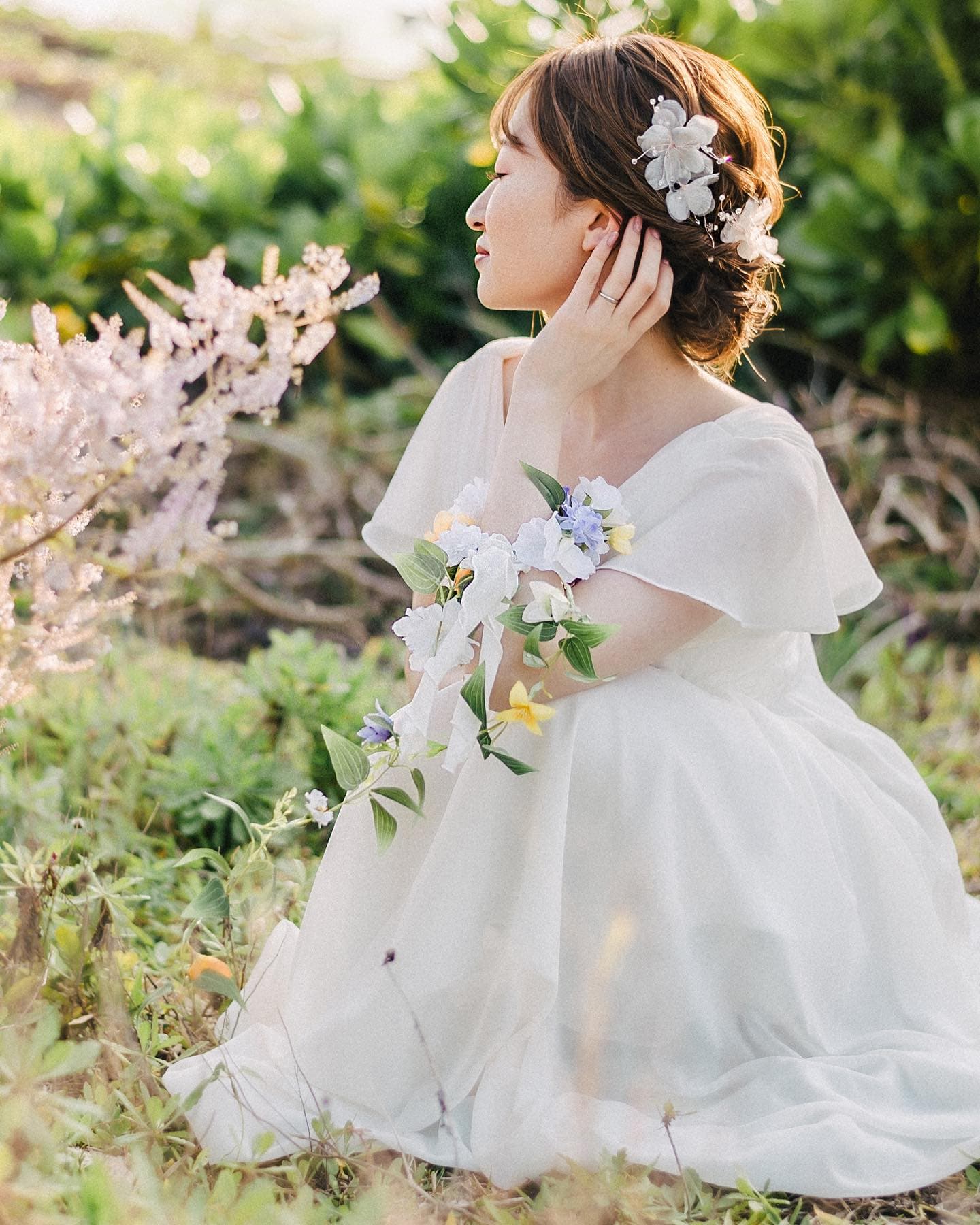 Bride in profile with blossoms in her hair, seated among spring greenery in Okinawa