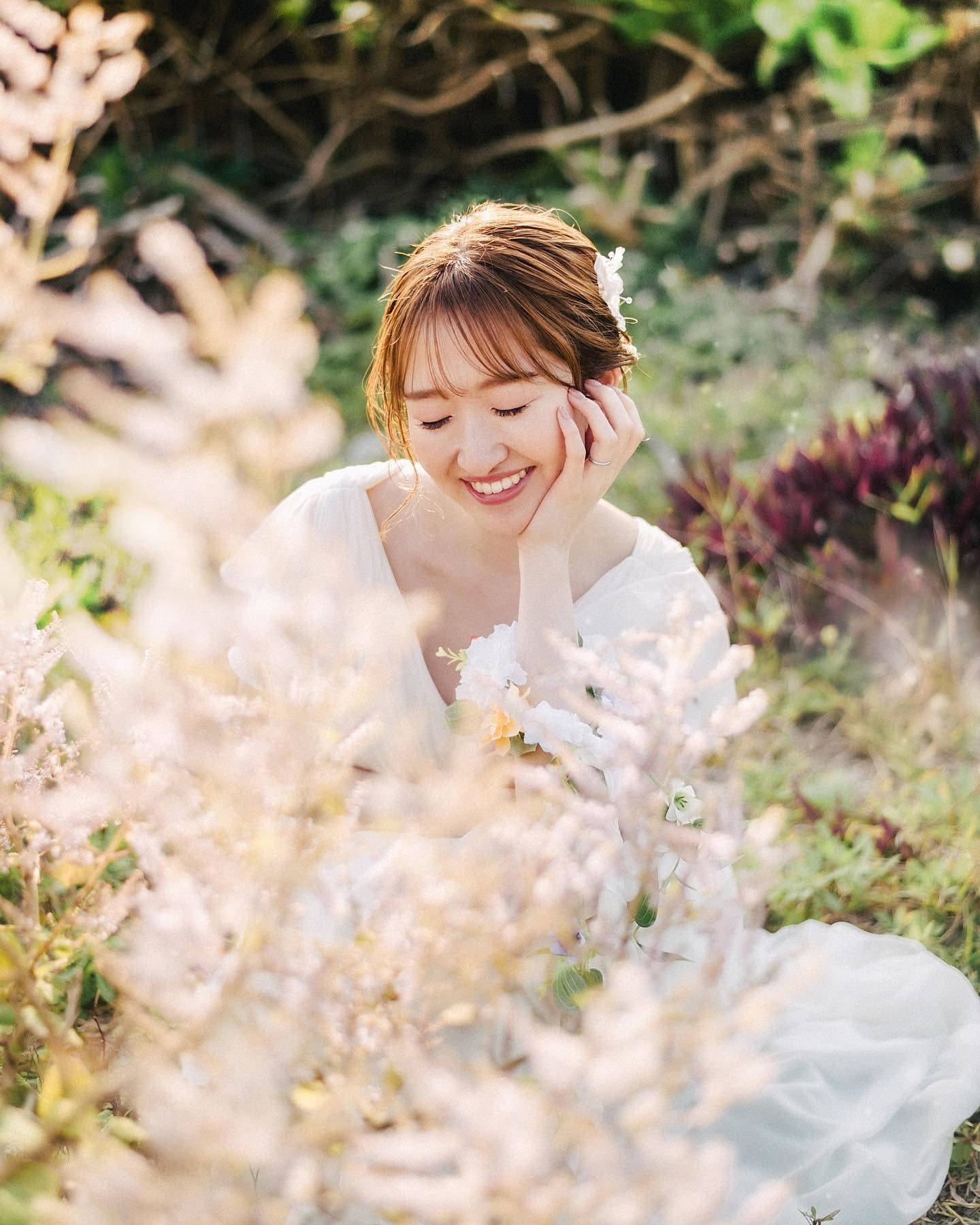 Smiling bride resting her chin on her hand amid soft spring grasses in Okinawa