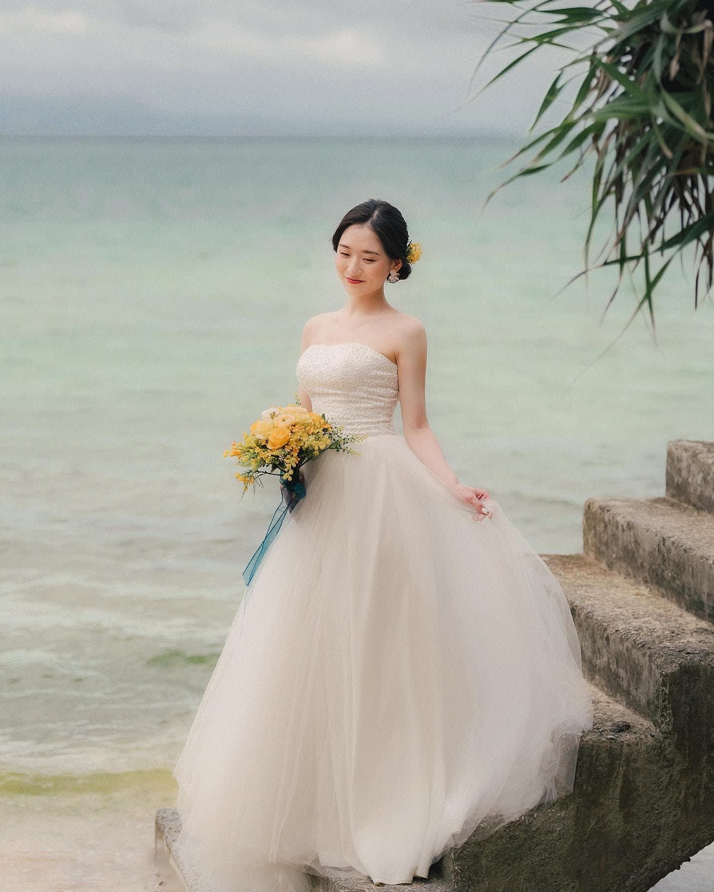 Bride in a tulle gown with a yellow bouquet by Okinawa's calm sea