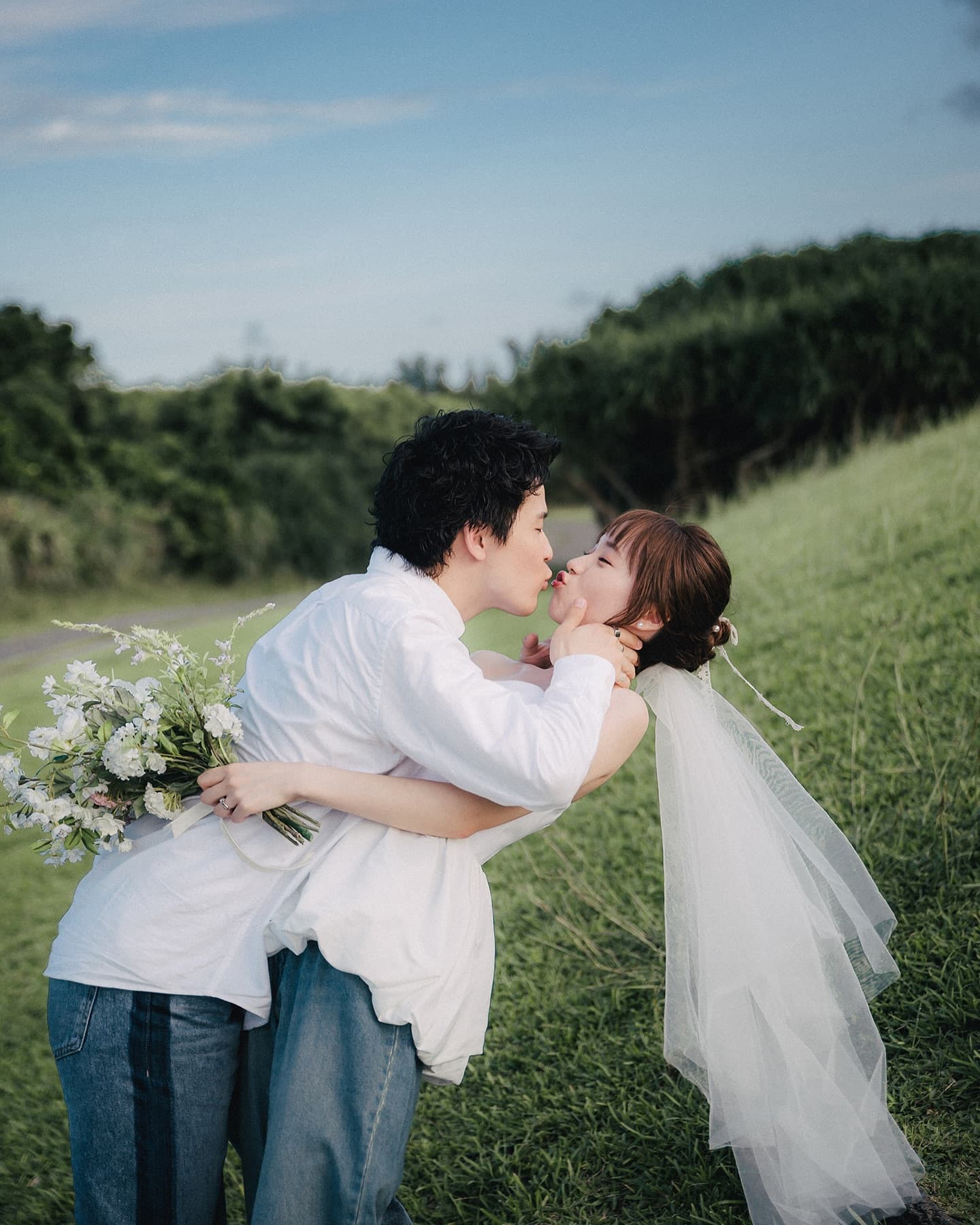 Couple kissing on an Okinawa hillside, long veil and white bouquet