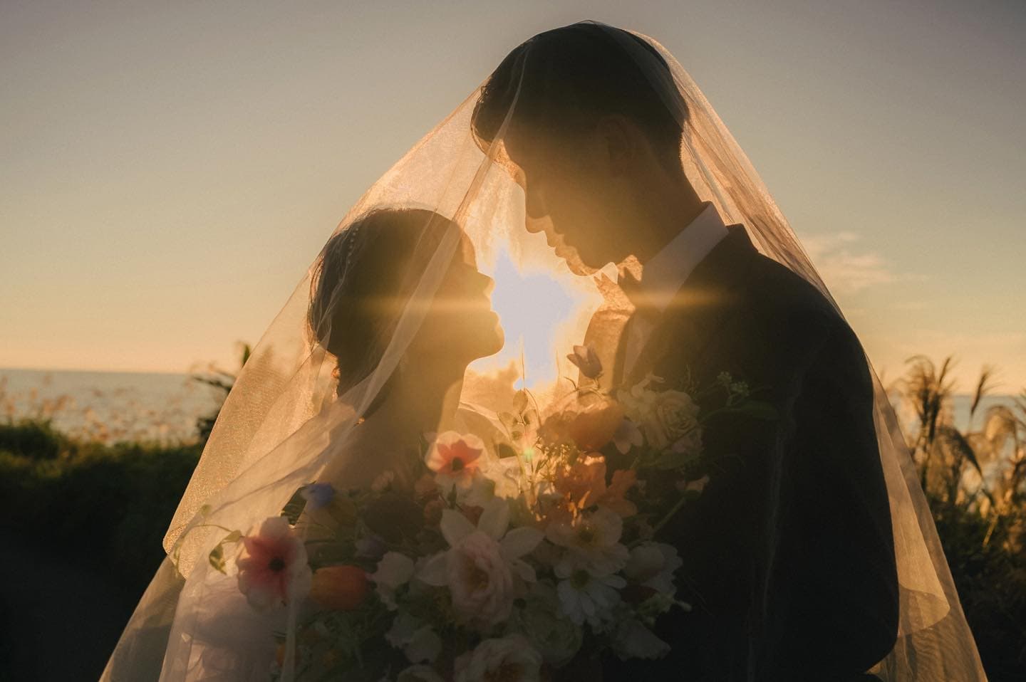Couple face to face beneath a glowing veil as the sun sets in Okinawa