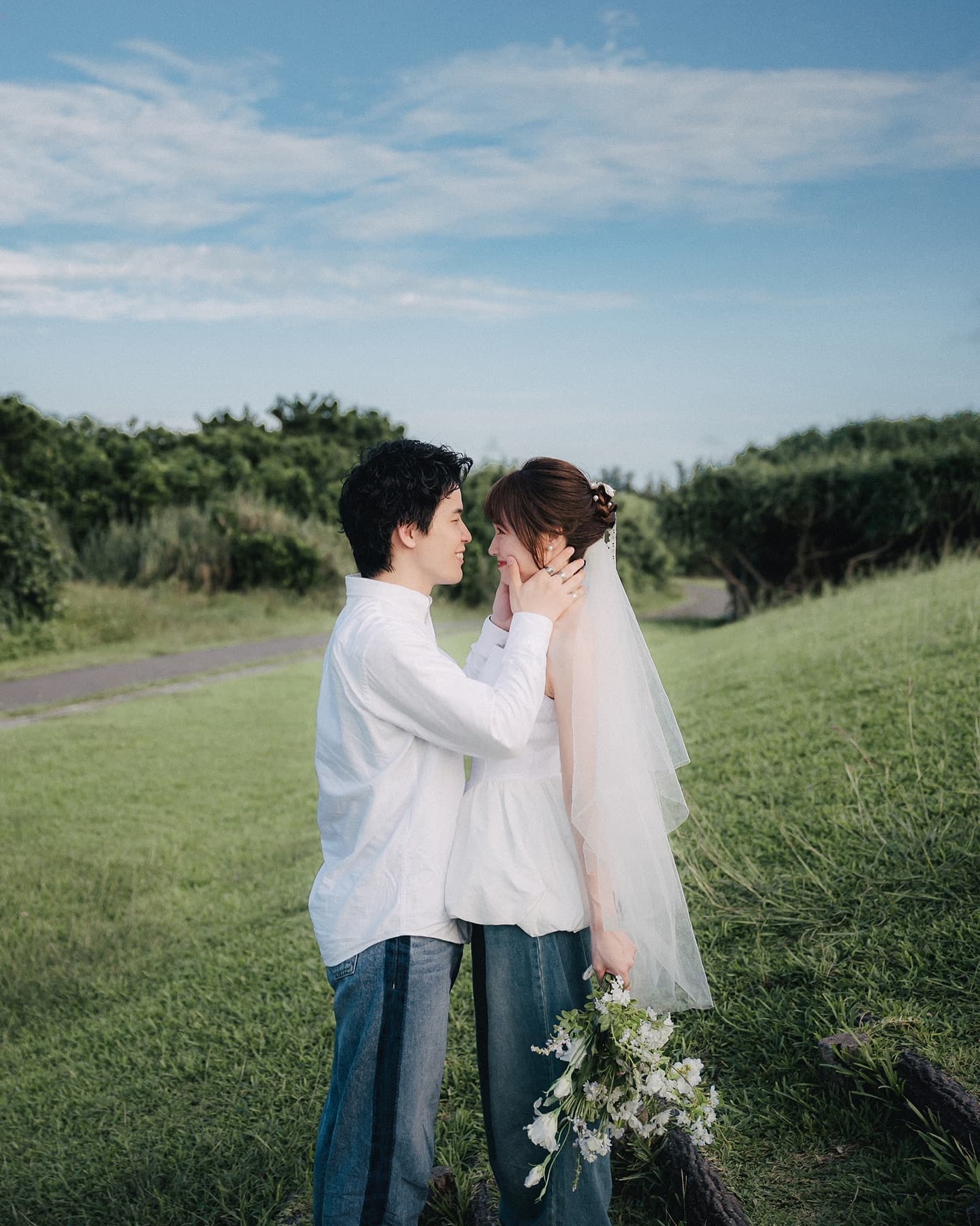 Groom cradling the bride's face on a green hill in Okinawa