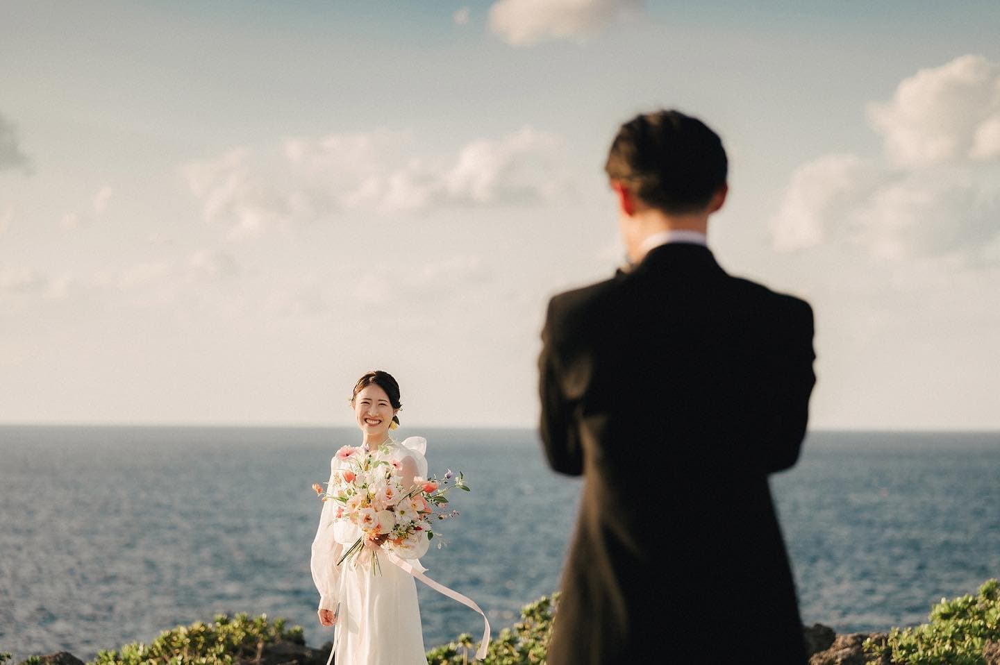 海辺の丘で新郎を見つめ微笑む新婦