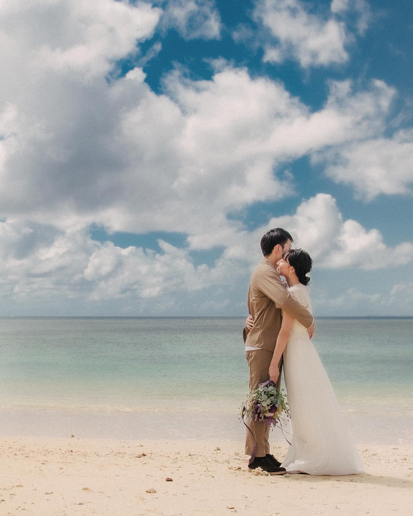 青い空と海を背に砂浜で抱き合う新郎新婦