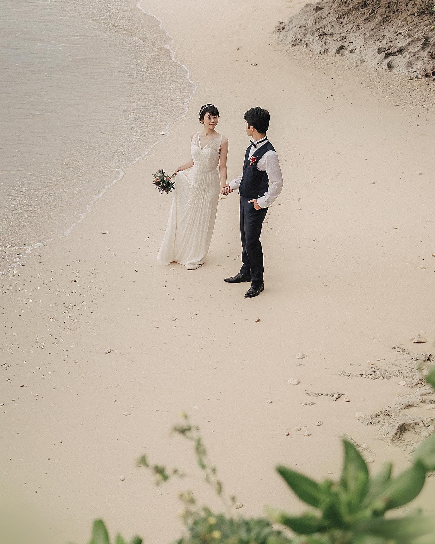 Bird's-eye view of a couple holding hands on the sand at the water's edge in Okinawa