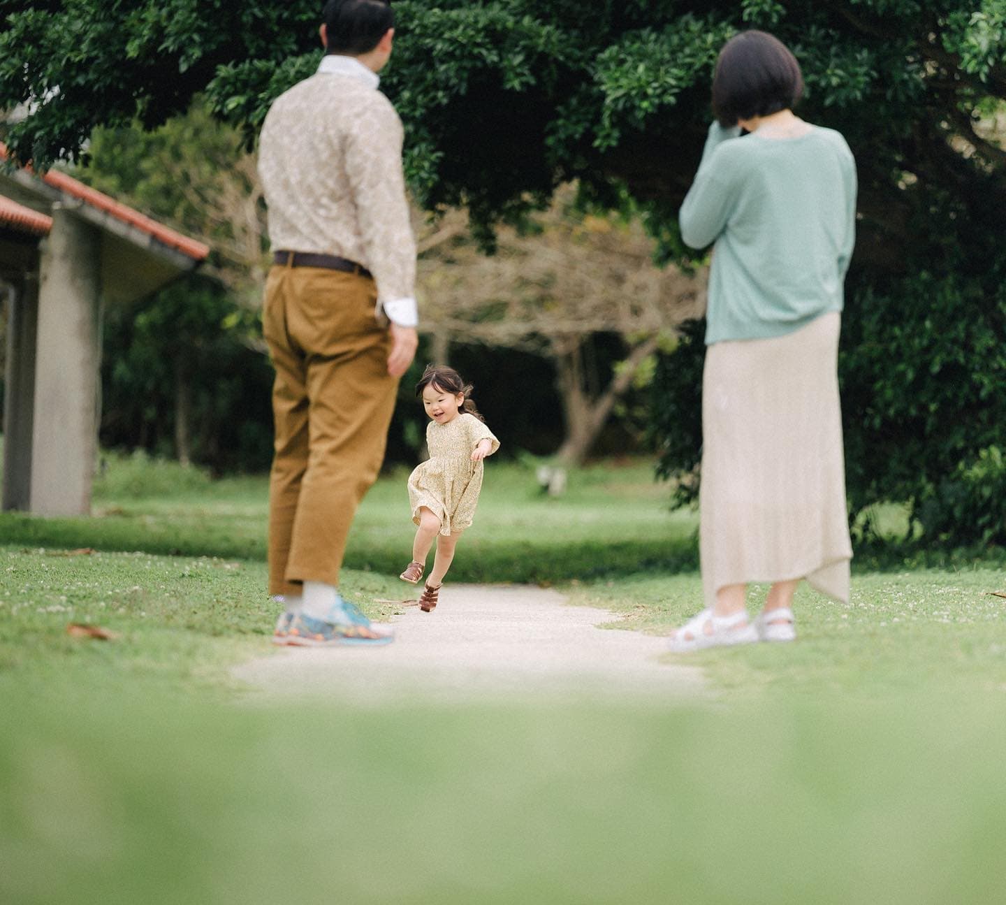 緑の公園で両親の間を元気に駆ける女の子