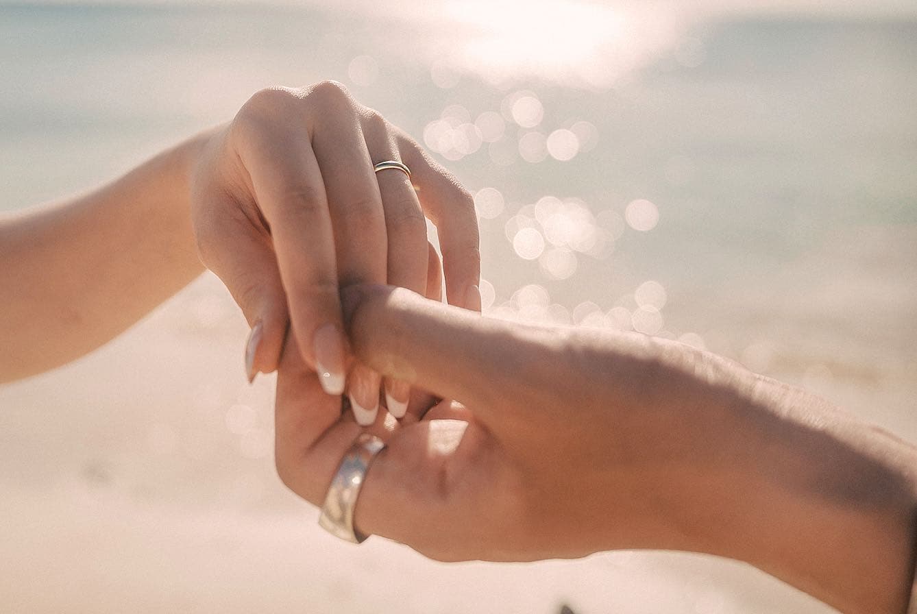 きらめく沖縄の海を背景に結婚指輪をつけた二人の手のクローズアップ