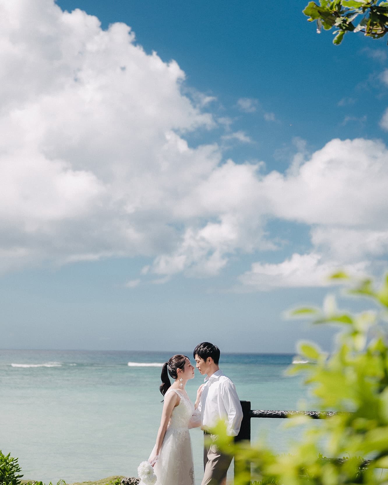 Bride and groom face to face by the sea under a wide Okinawa sky
