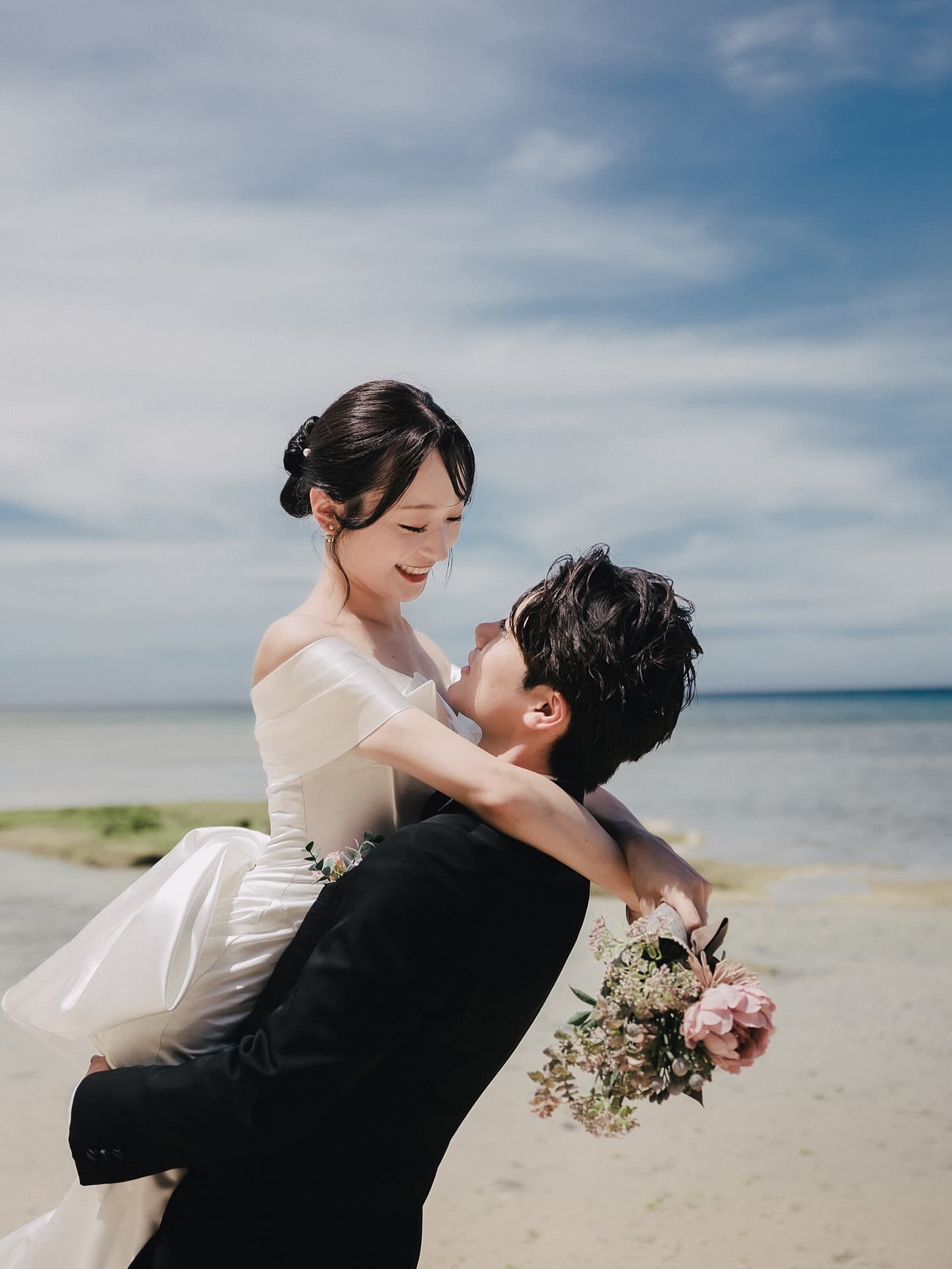 Groom lifting his bride on a beach under a bright blue Okinawa sky