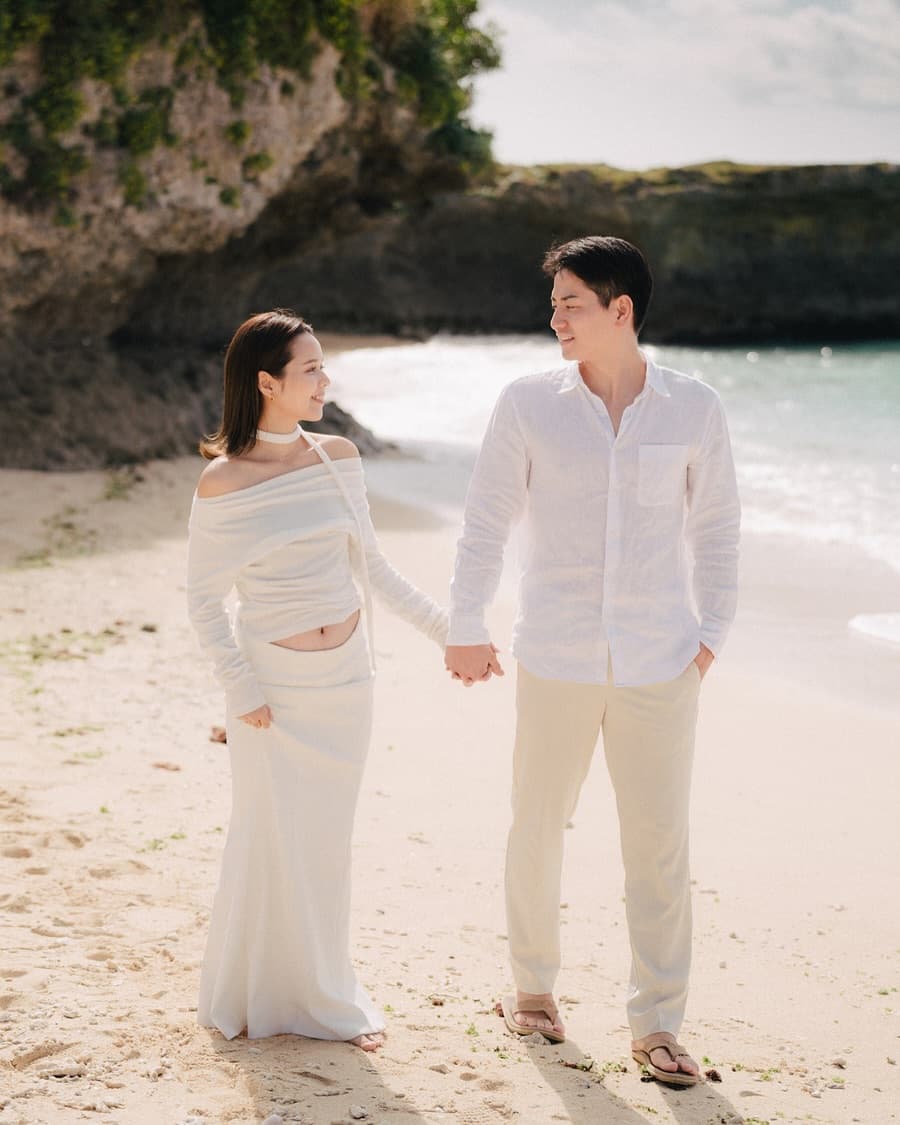 Expecting couple holding hands and smiling on a sunny rocky beach in Okinawa