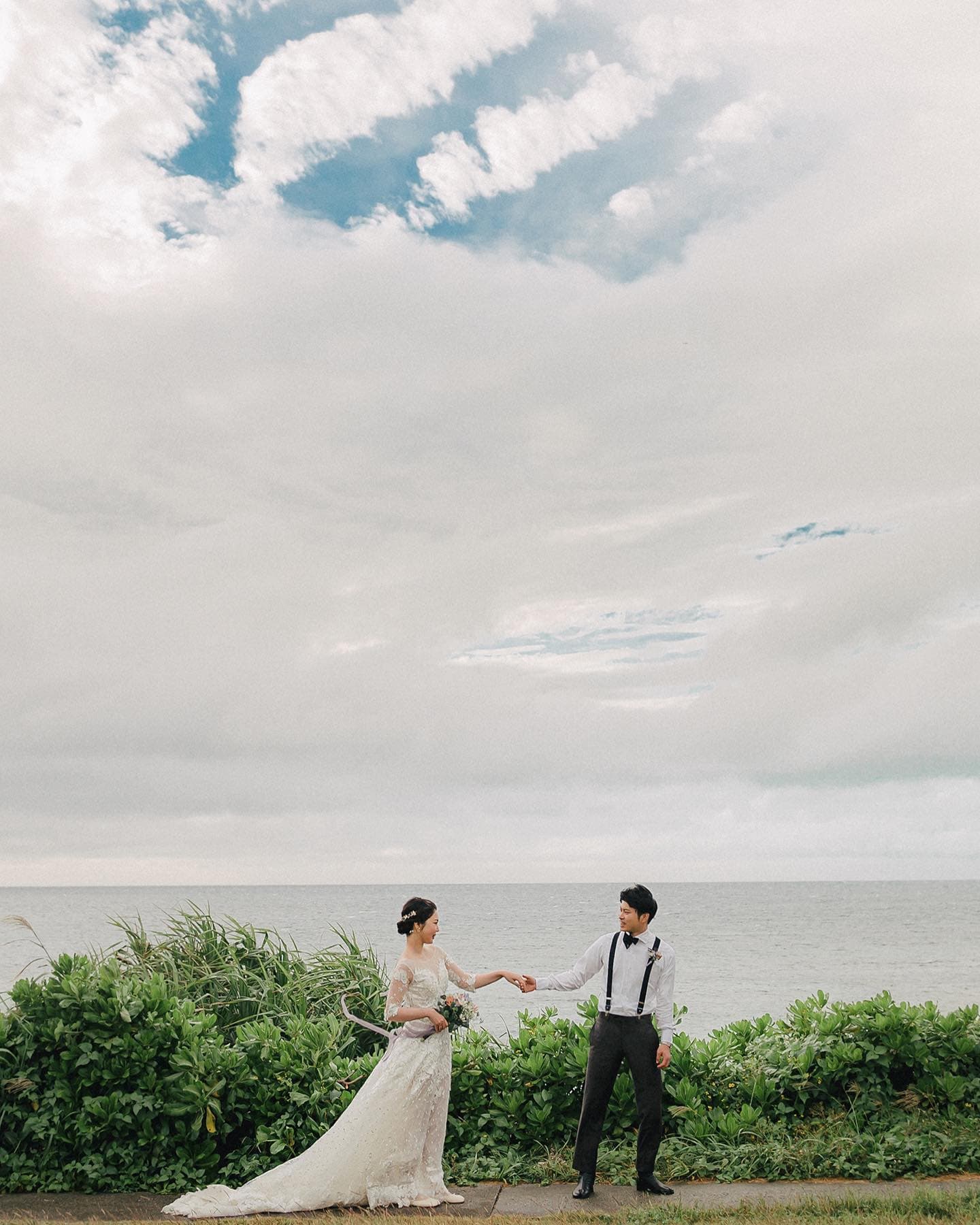 Couple reaching for each other's hands on a seaside path under a wide cloudy sky in Okinawa.