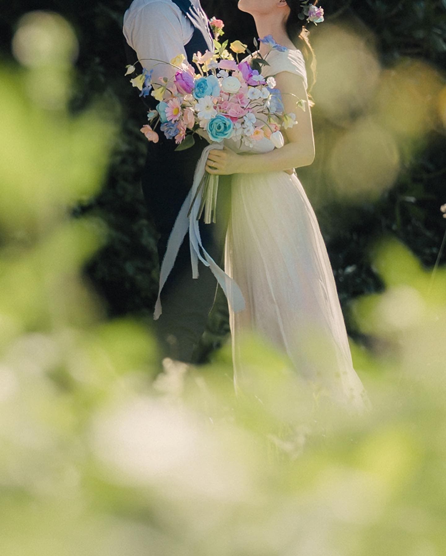 Bride in a white dress holding a pastel bouquet, framed by soft green bokeh