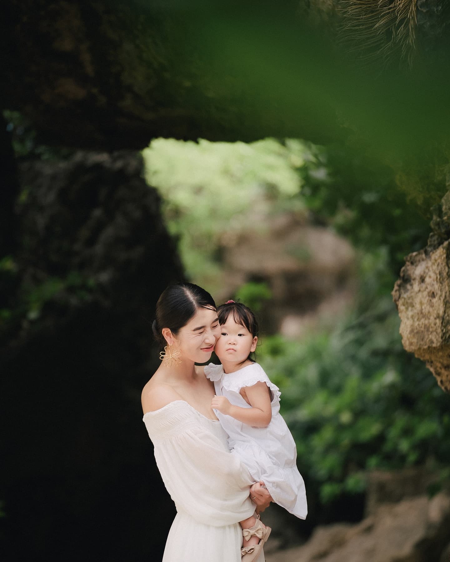 Mother in a white dress holding her girl among Okinawa greenery