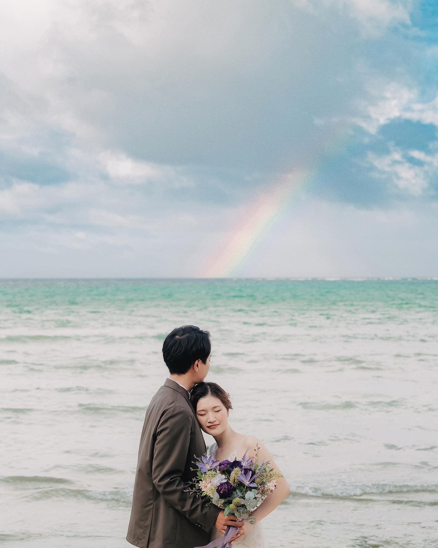 虹がかかる沖縄の海を背に抱き合う新郎新婦