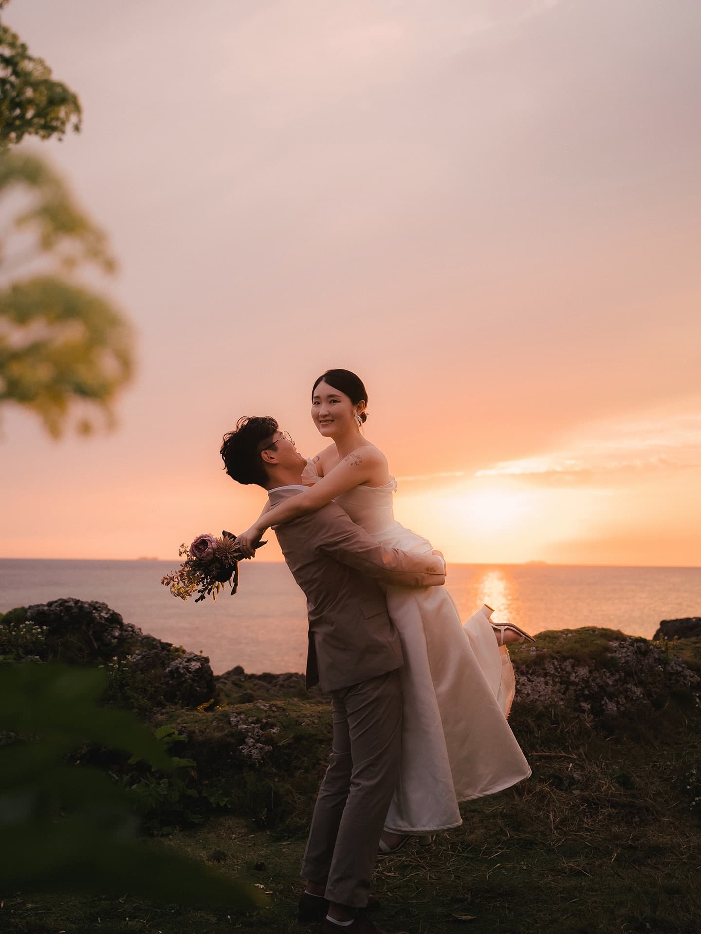 Groom lifting his bride against the sunset sea in Okinawa