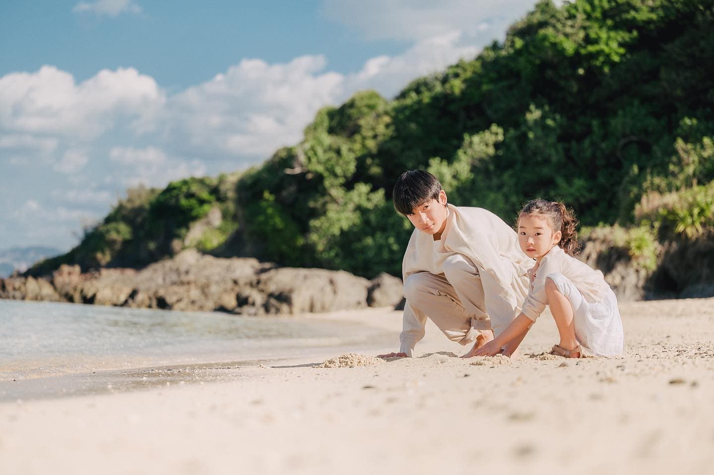 沖縄の砂浜で娘と一緒に砂遊びをする父親
