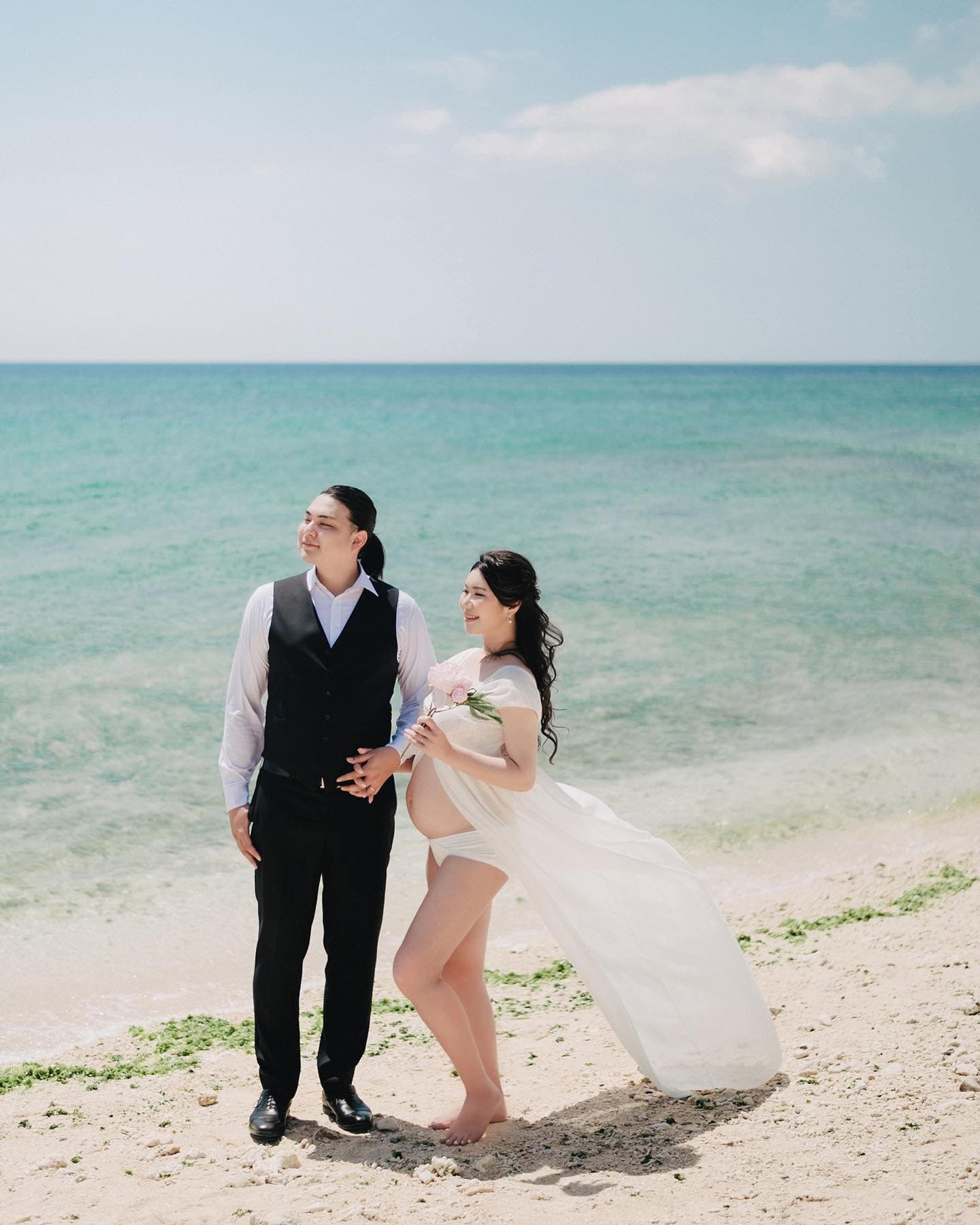 Expectant couple standing on an Okinawa beach against clear sea and sky