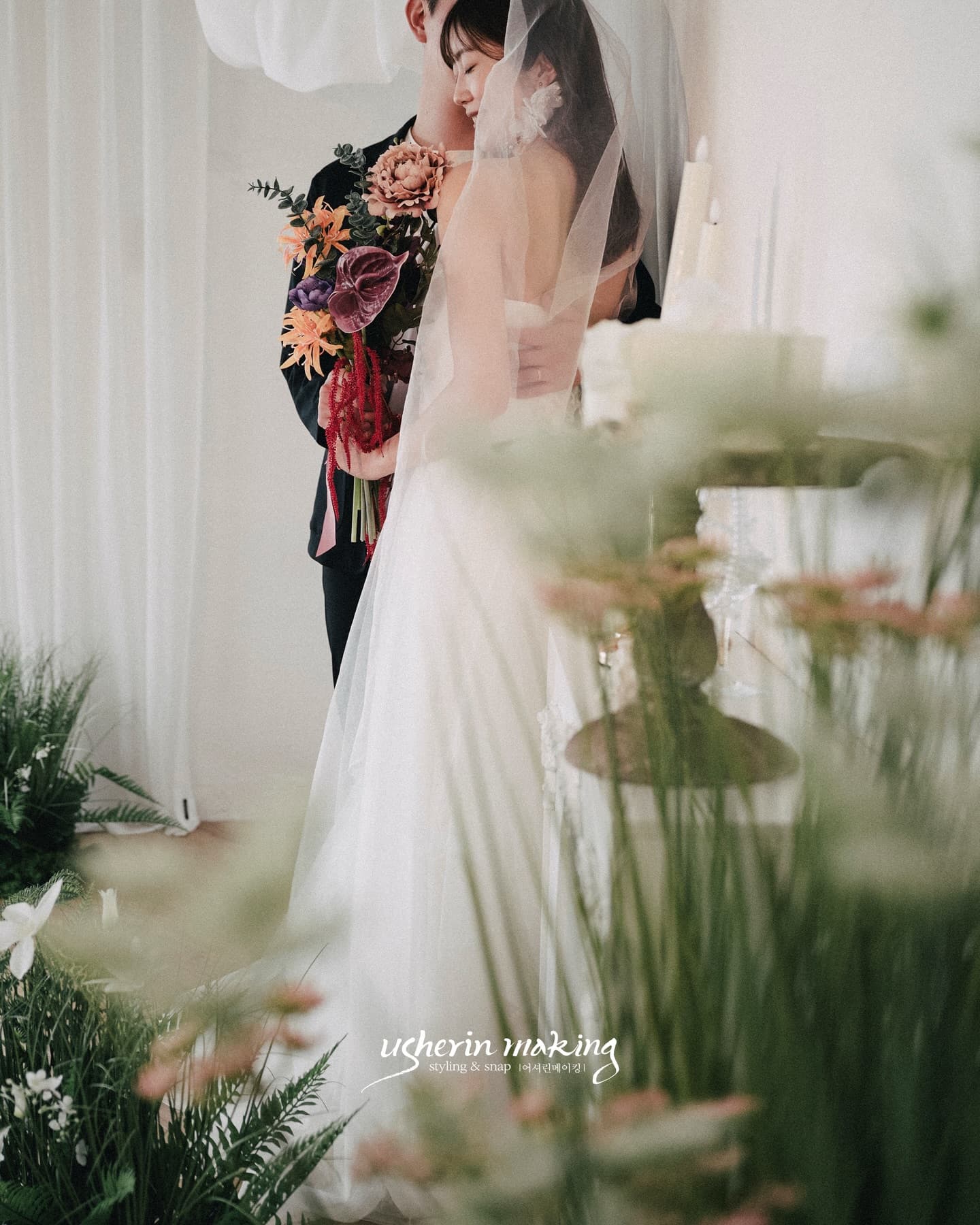 Bride in a long veil embracing the groom holding a colorful bouquet in the studio