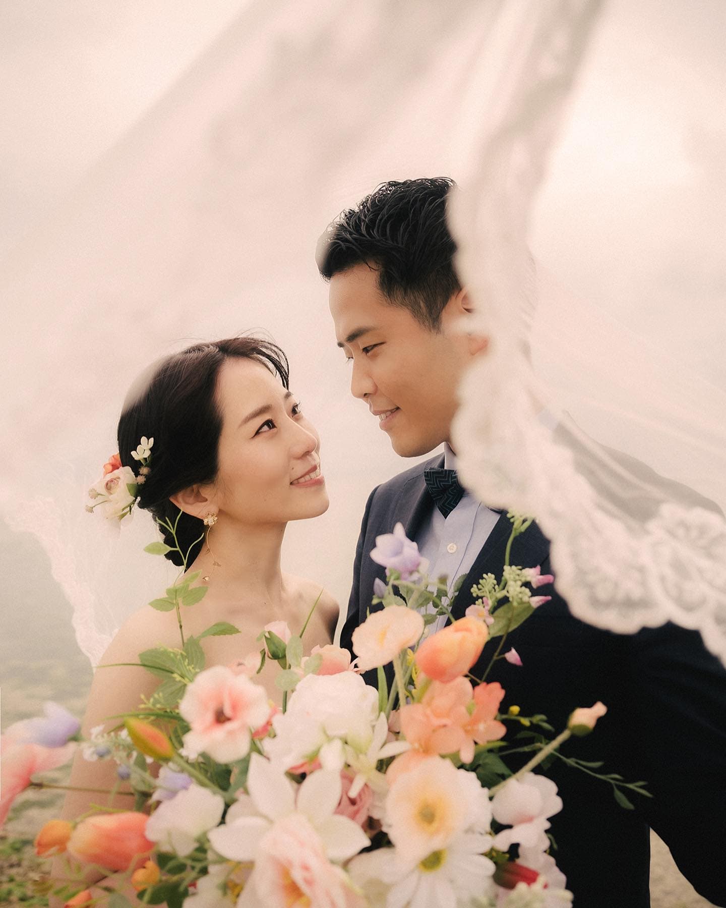 ベールに包まれ見つめ合う新郎新婦とパステルのブーケ