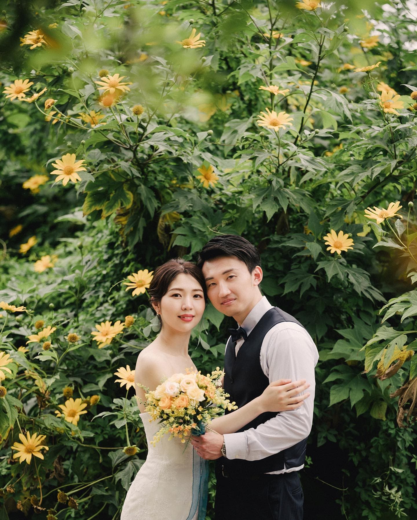 Bride and groom smiling at the camera before a wall of yellow flowers in Okinawa