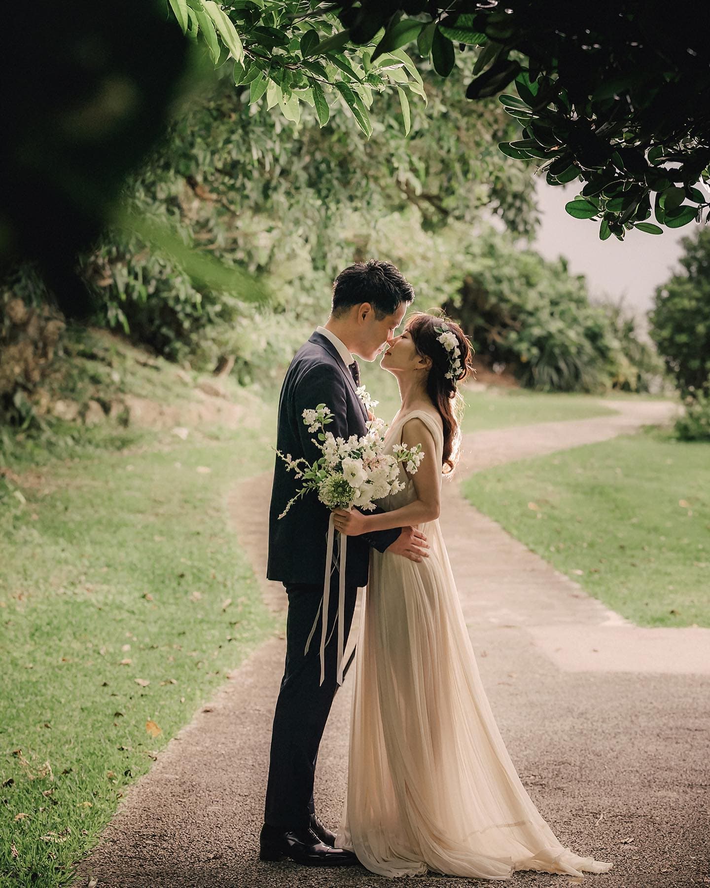 Bride and groom sharing a kiss beneath overhanging green branches