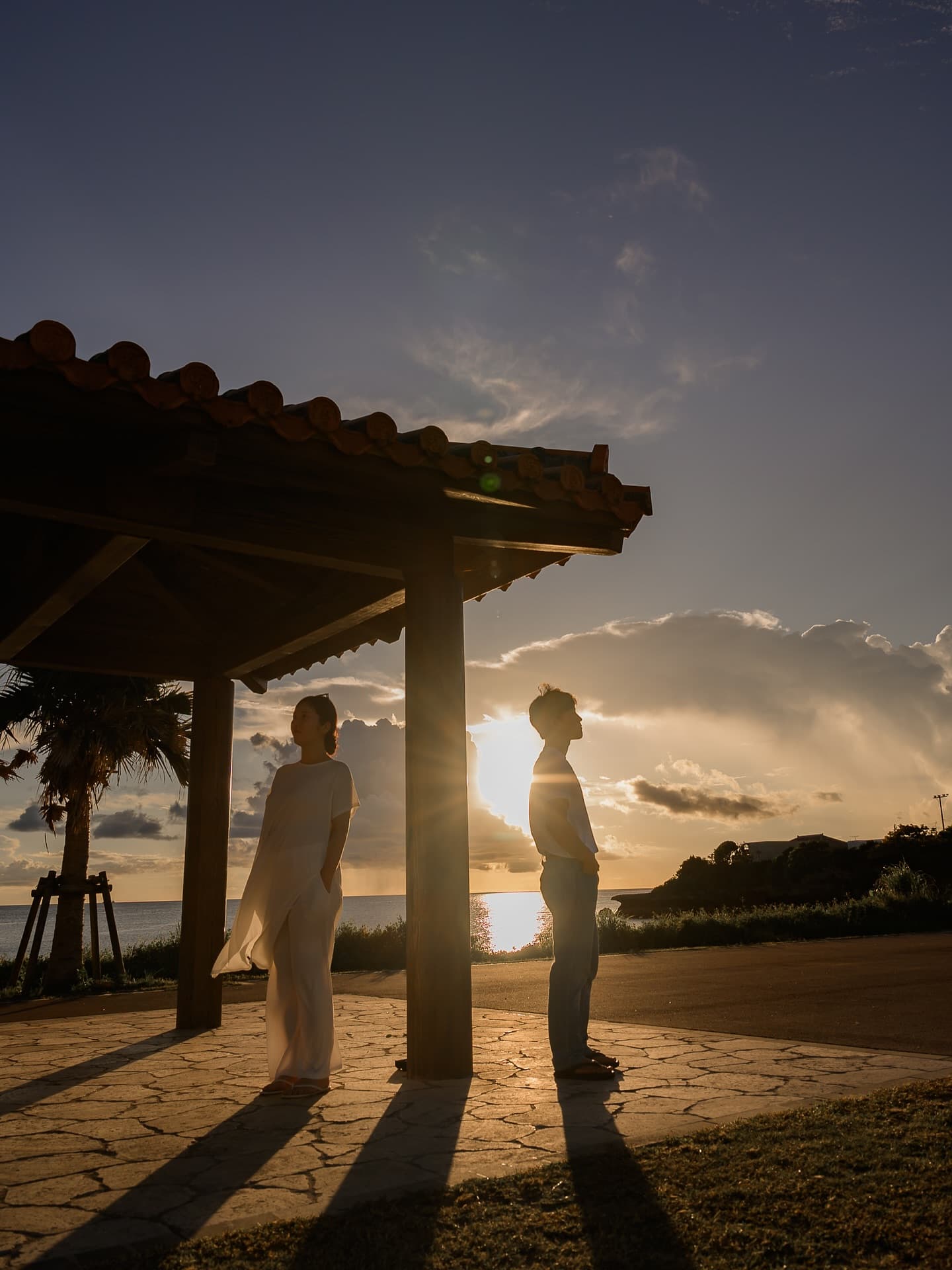 Couple facing each other at sunset by a red-tiled pavilion in Okinawa