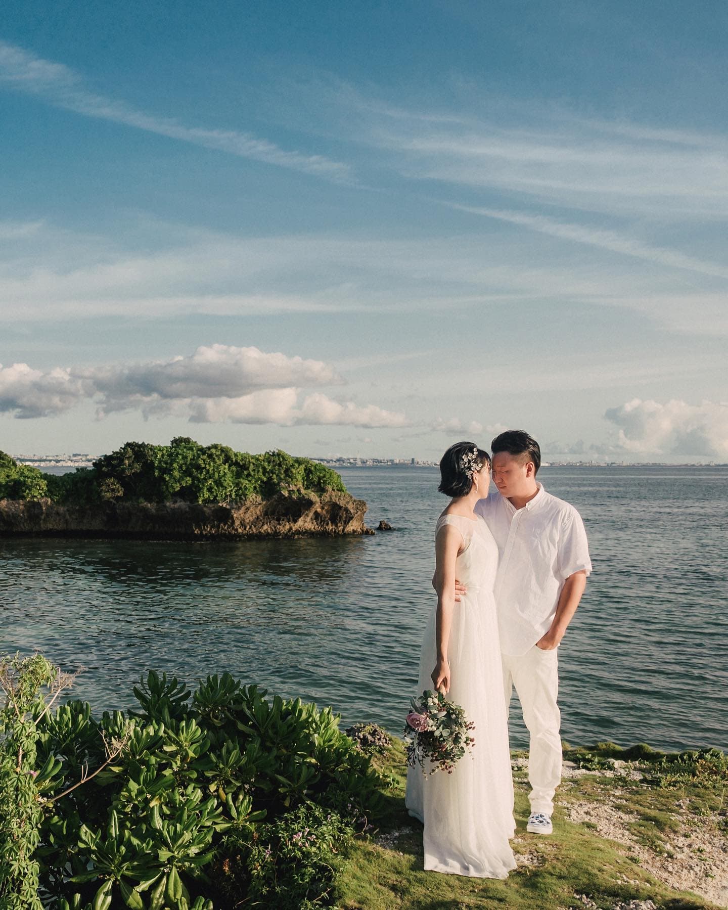 Couple face to face on a green headland above the blue Okinawa sea