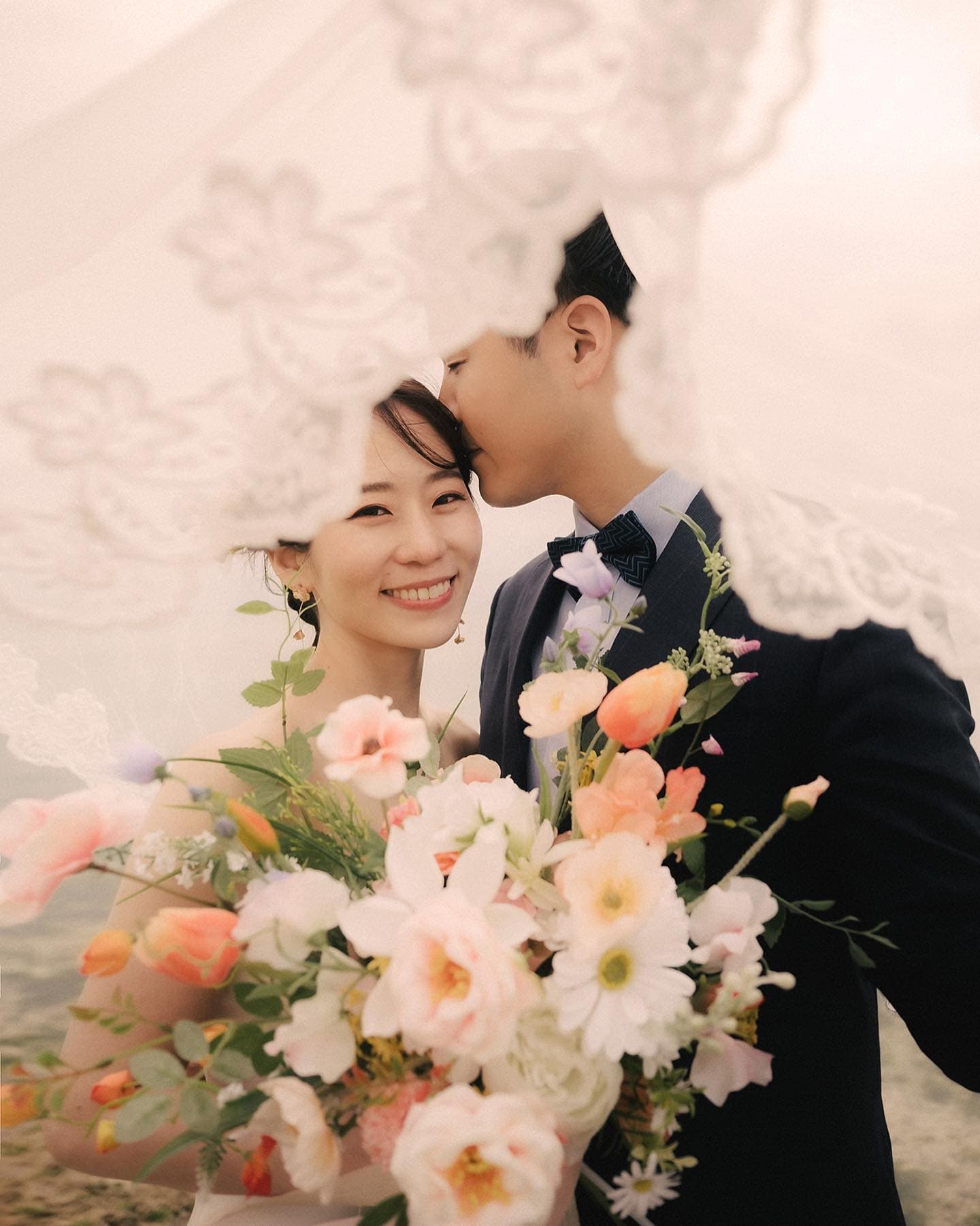 レースのベール越しに新婦の額にキスをする新郎