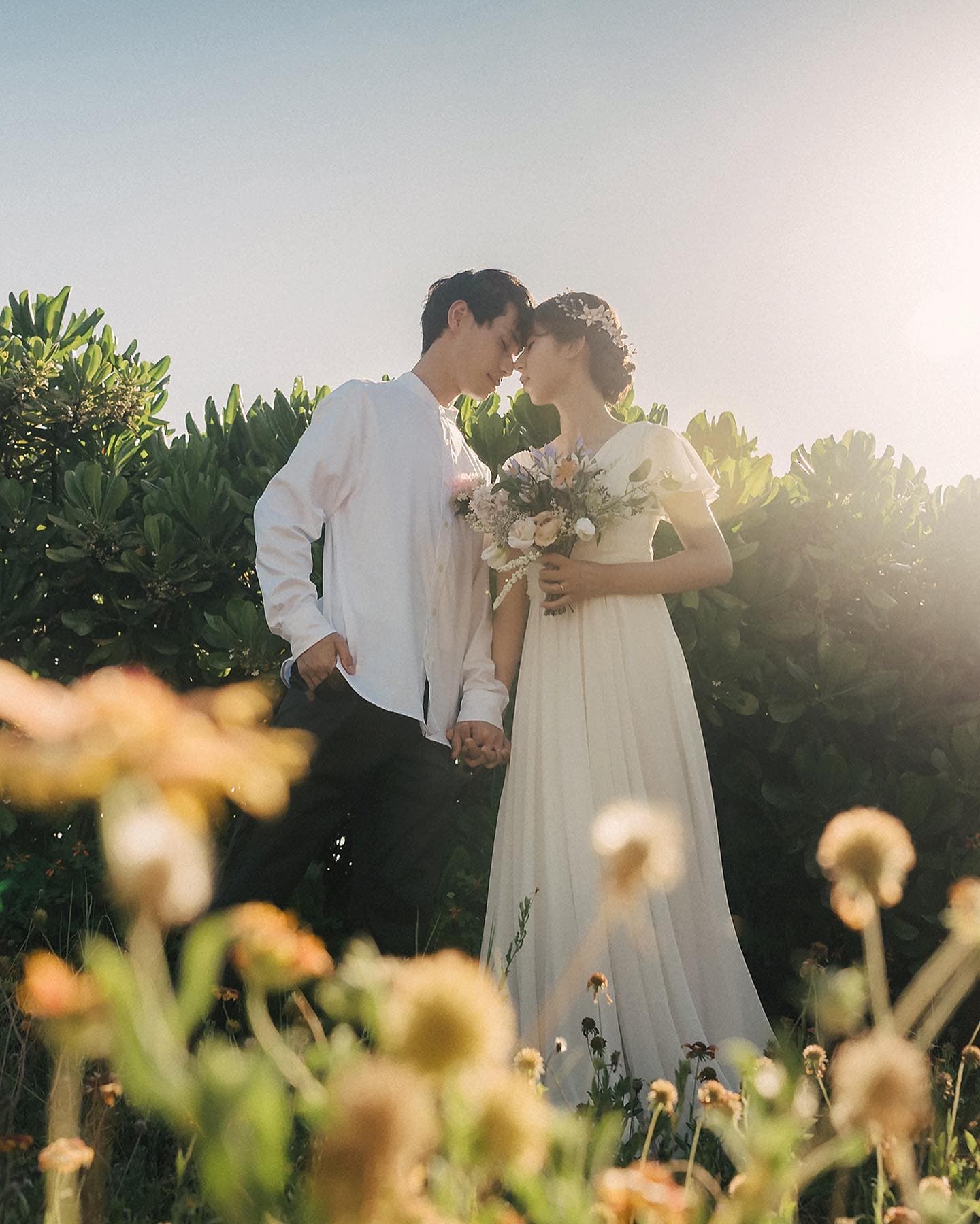 Couple standing close among wildflowers in warm summer backlight in Okinawa