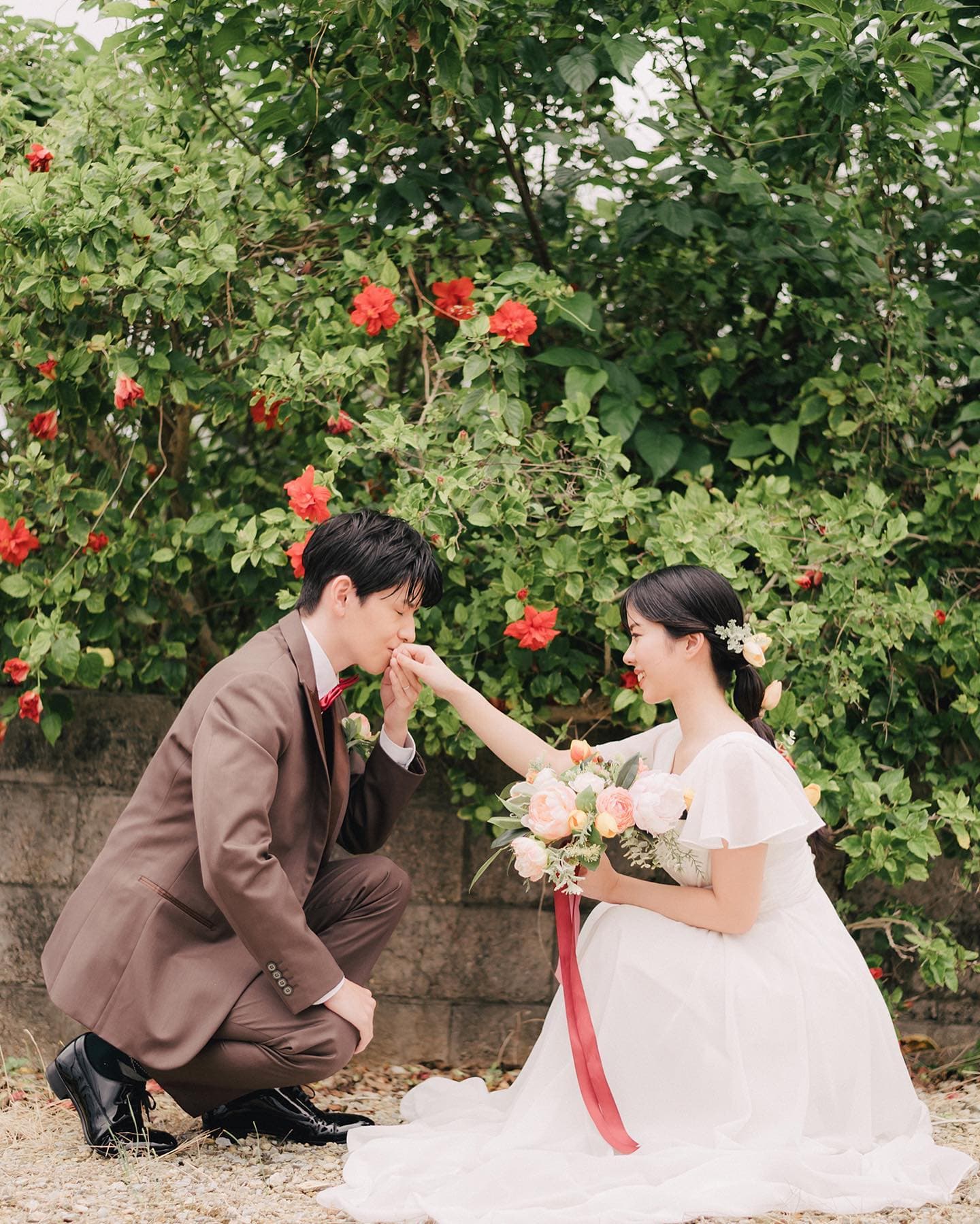 붉은 히비스커스 앞에서 신부의 손에 입 맞추는 신랑, 오키나와