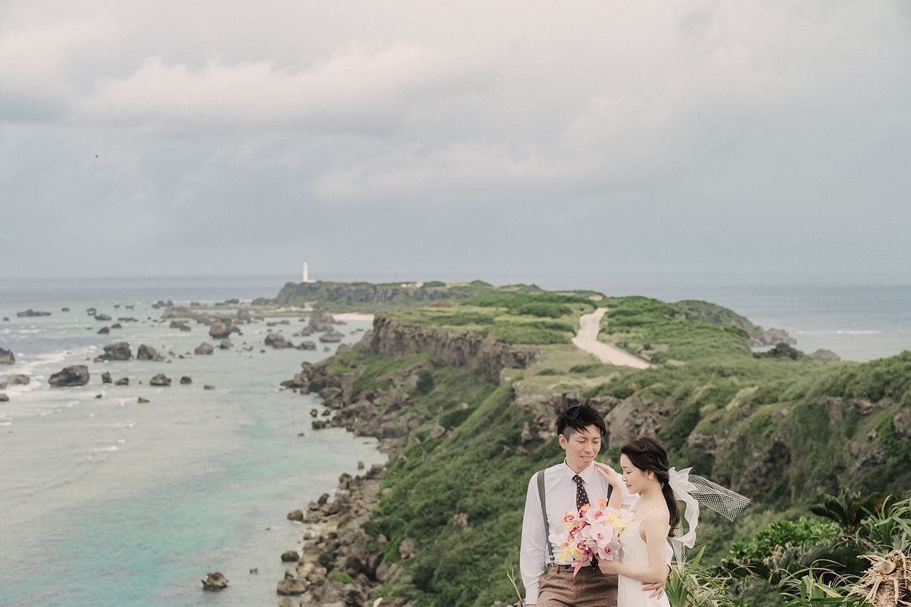 Couple standing on a bluff over the Miyakojima coastline under an overcast sky