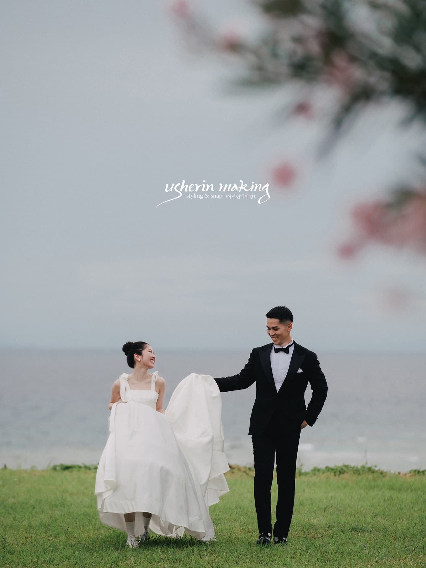 Couple smiling on a seaside lawn as the groom holds her dress in Okinawa