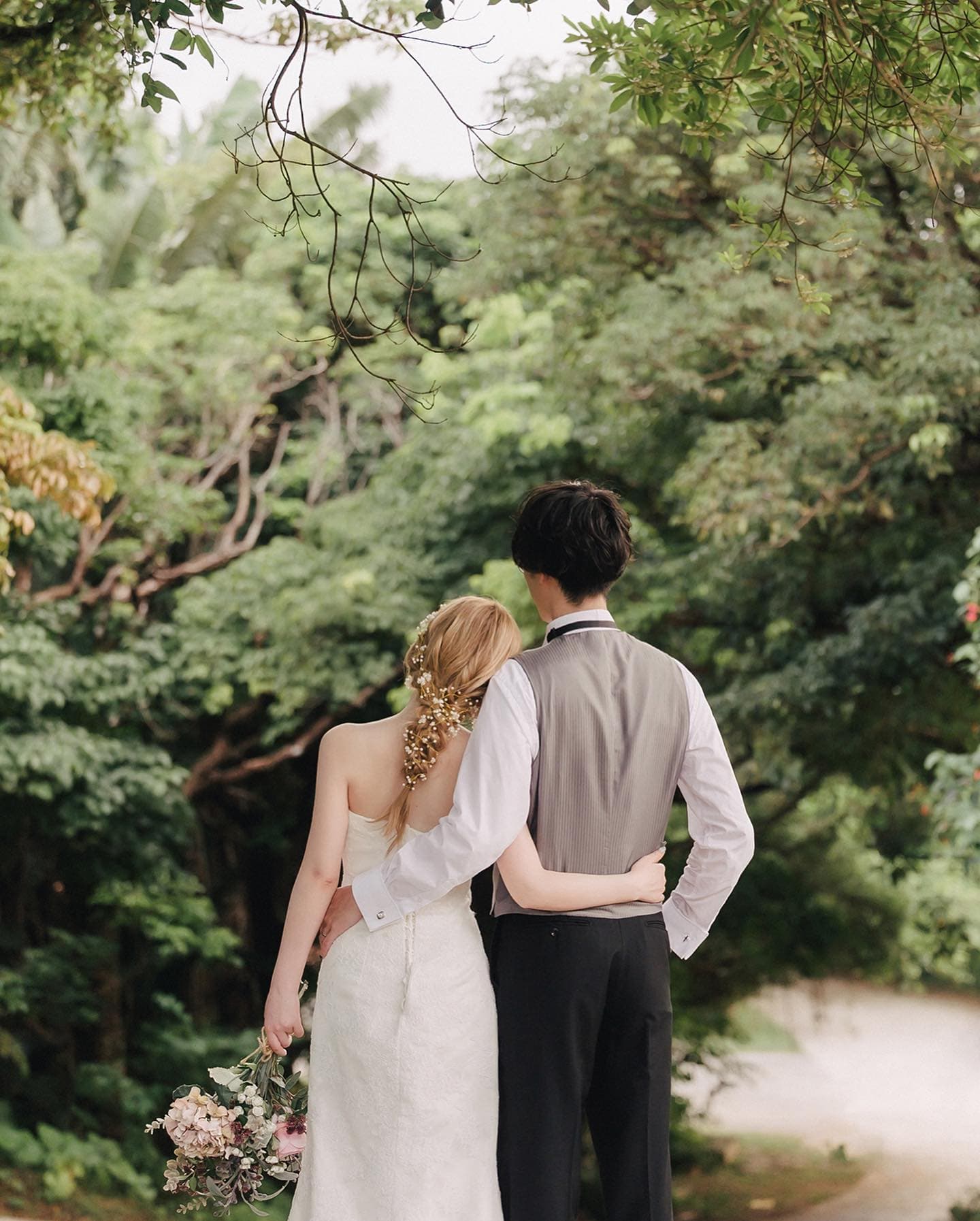 Back view of a couple arm in arm on a deep green forest path in Okinawa