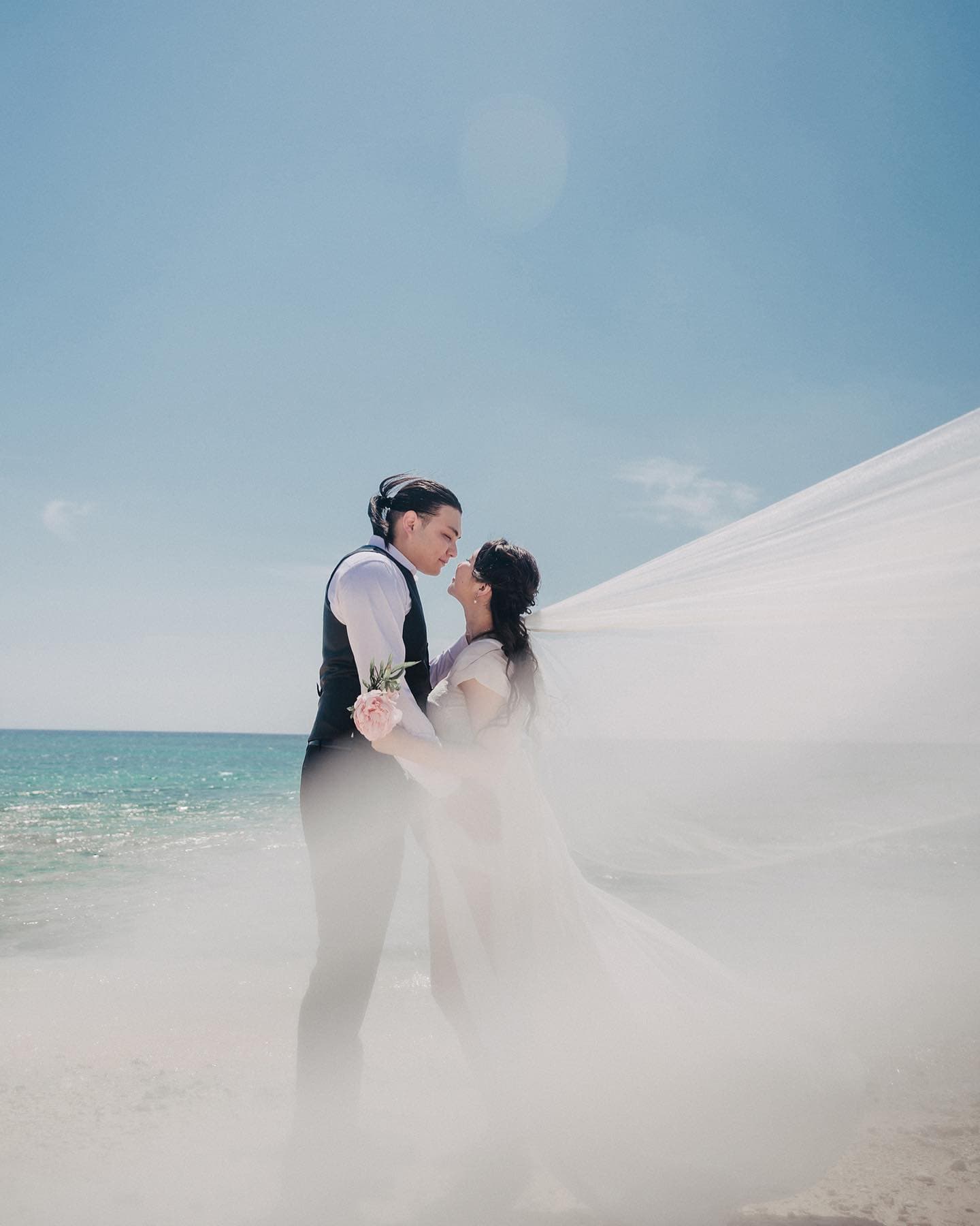 Couple gazing at each other on the beach as a long veil sweeps in the wind, Okinawa