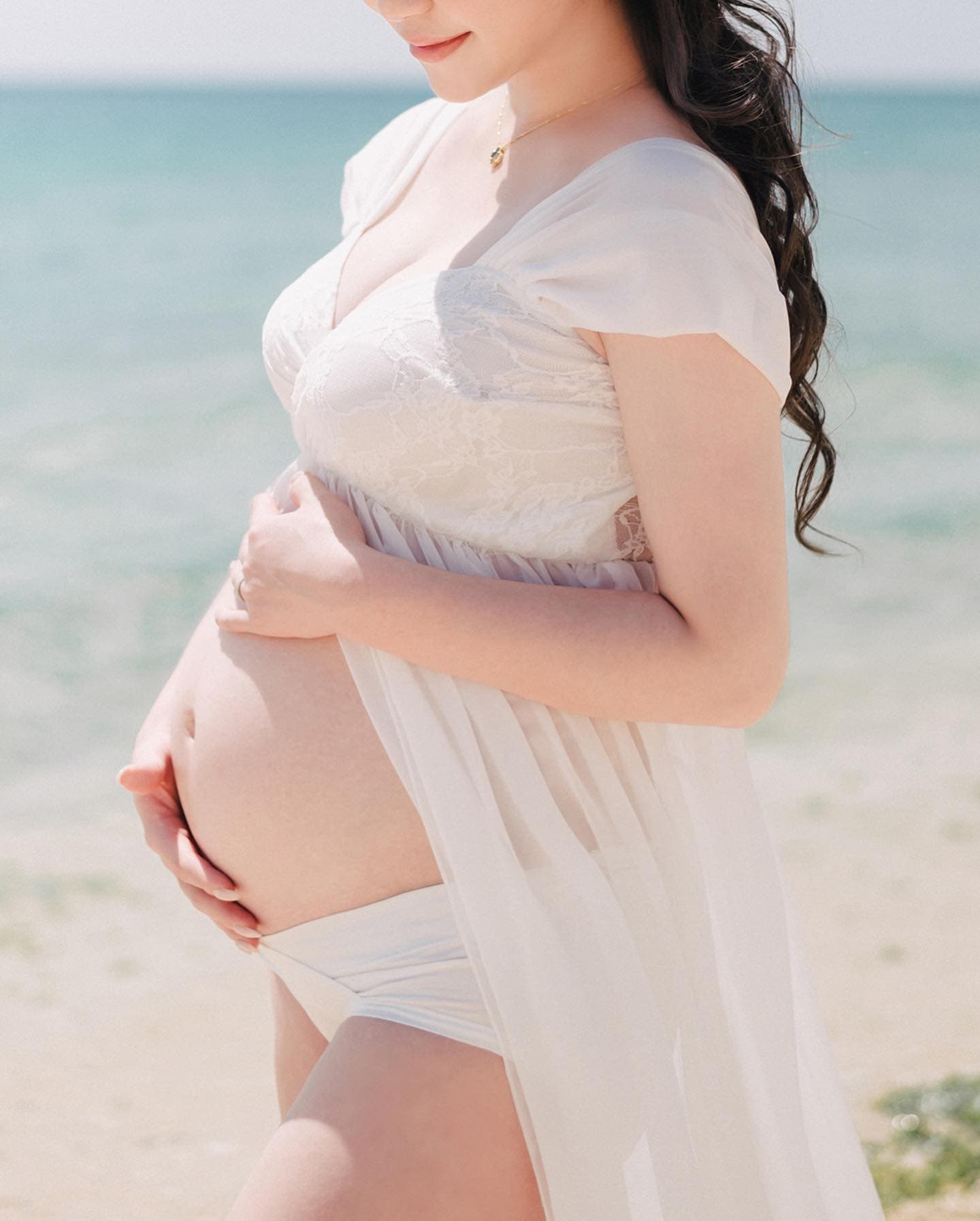 Close-up of a mother-to-be gently holding her baby bump by the sea in Okinawa