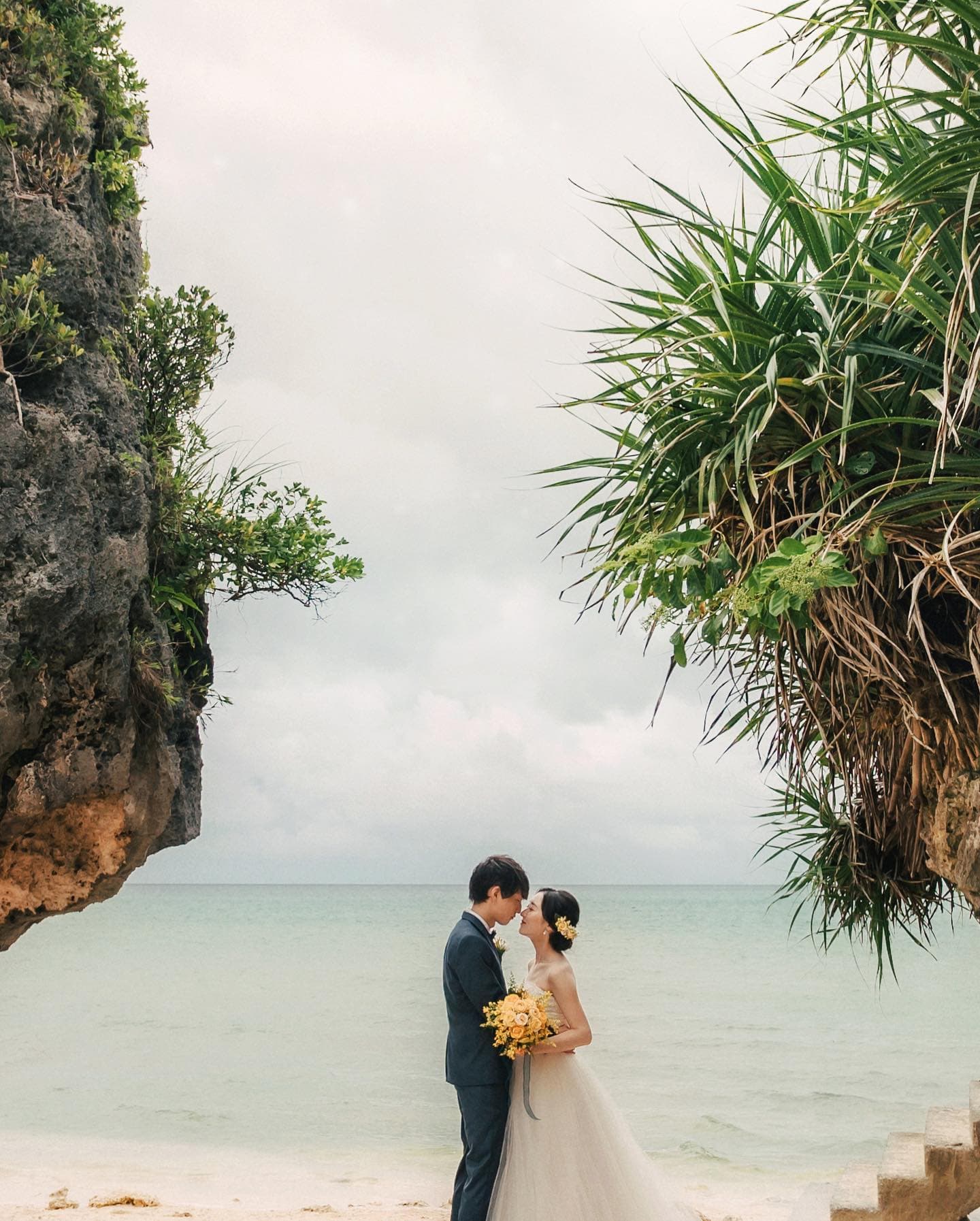 Bride and groom between sea cliffs on an overcast Okinawa beach