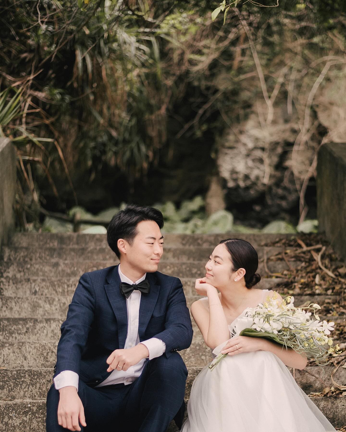 돌계단에 나란히 앉아 마주 웃는 신랑신부, 흐린 오키나와
