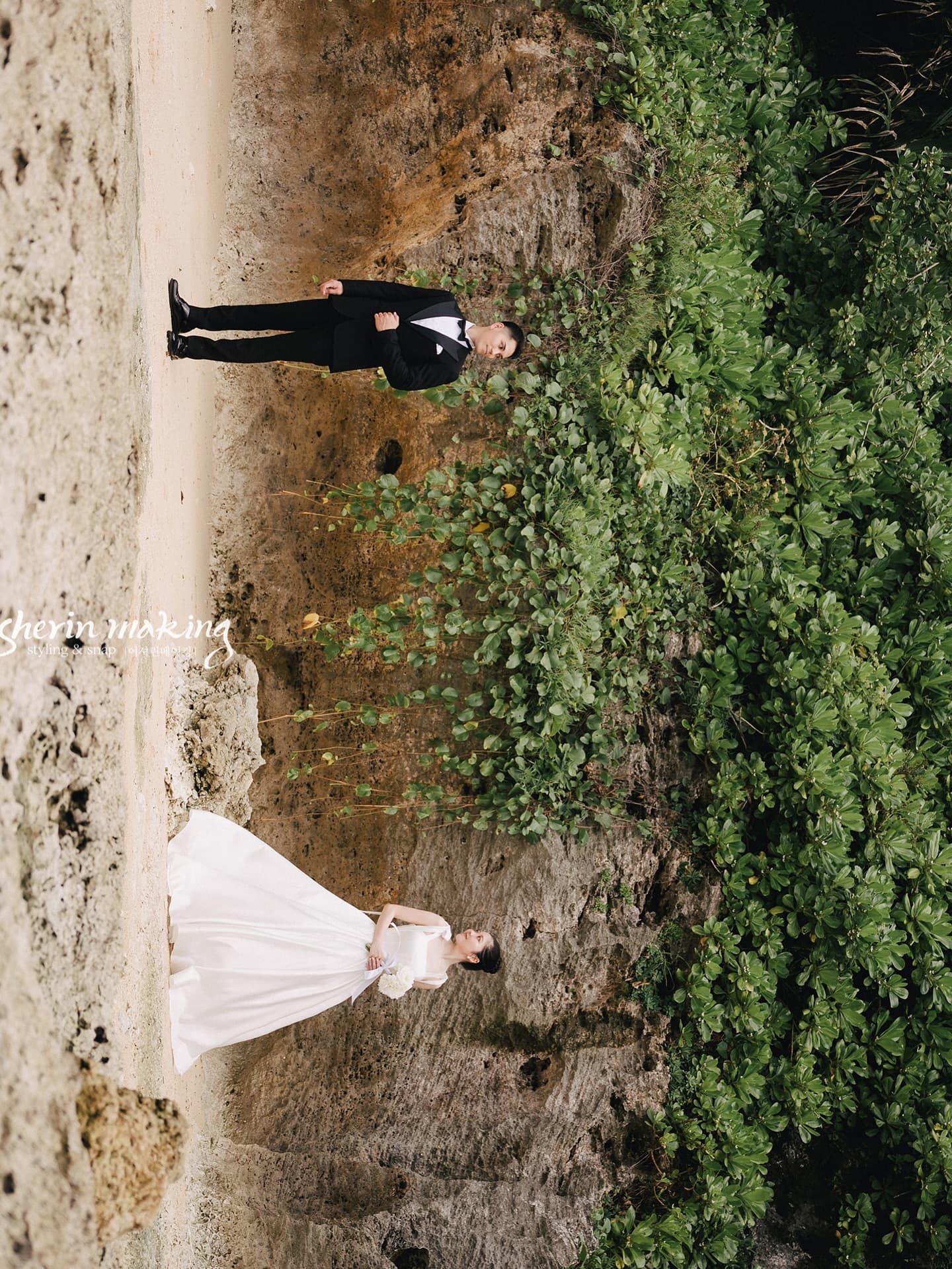 Bride and groom posing apart on a rocky green slope in Okinawa