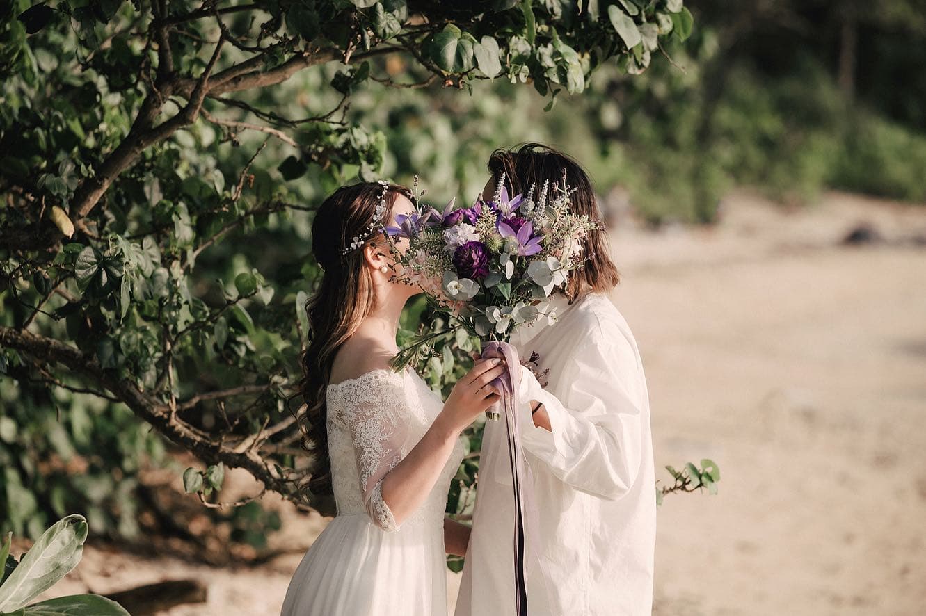Couple hiding a kiss behind a purple bouquet on an Okinawa beach