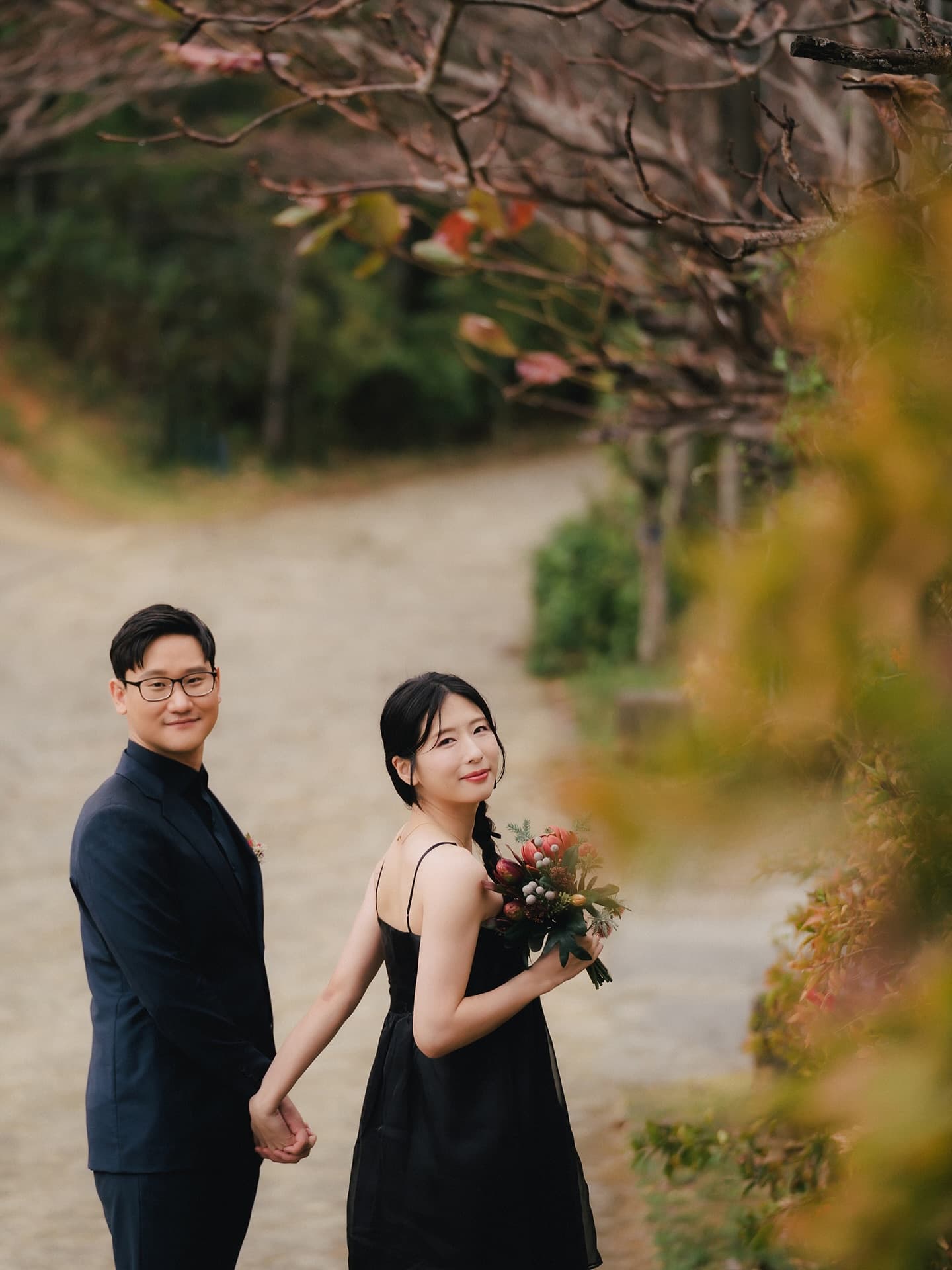 Couple in black holding hands on a tree-lined autumn path in Okinawa