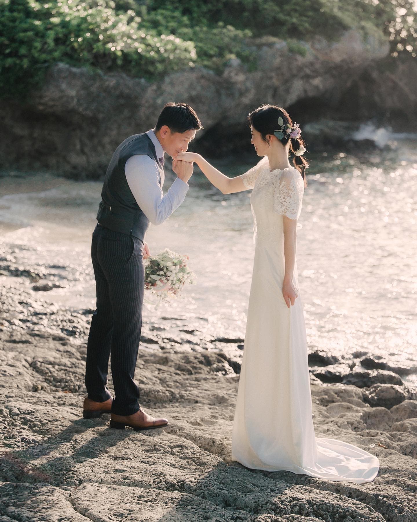 Groom kissing his bride's hand on a rocky Okinawa shore