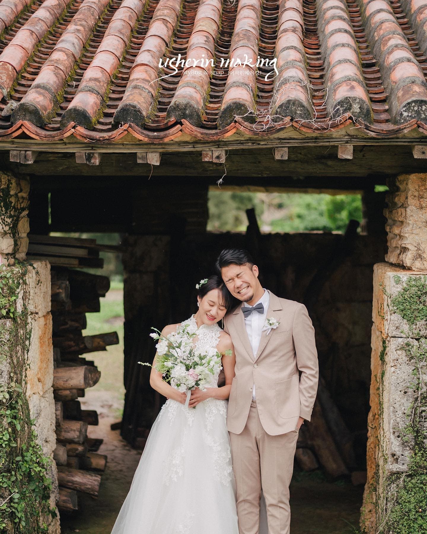 Bride and groom smile beneath the red-tiled gate of an old Okinawan folk house