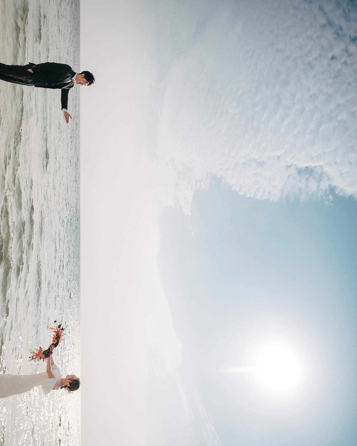 Groom playing in the surf while the bride holds her bouquet under bright Okinawa sun