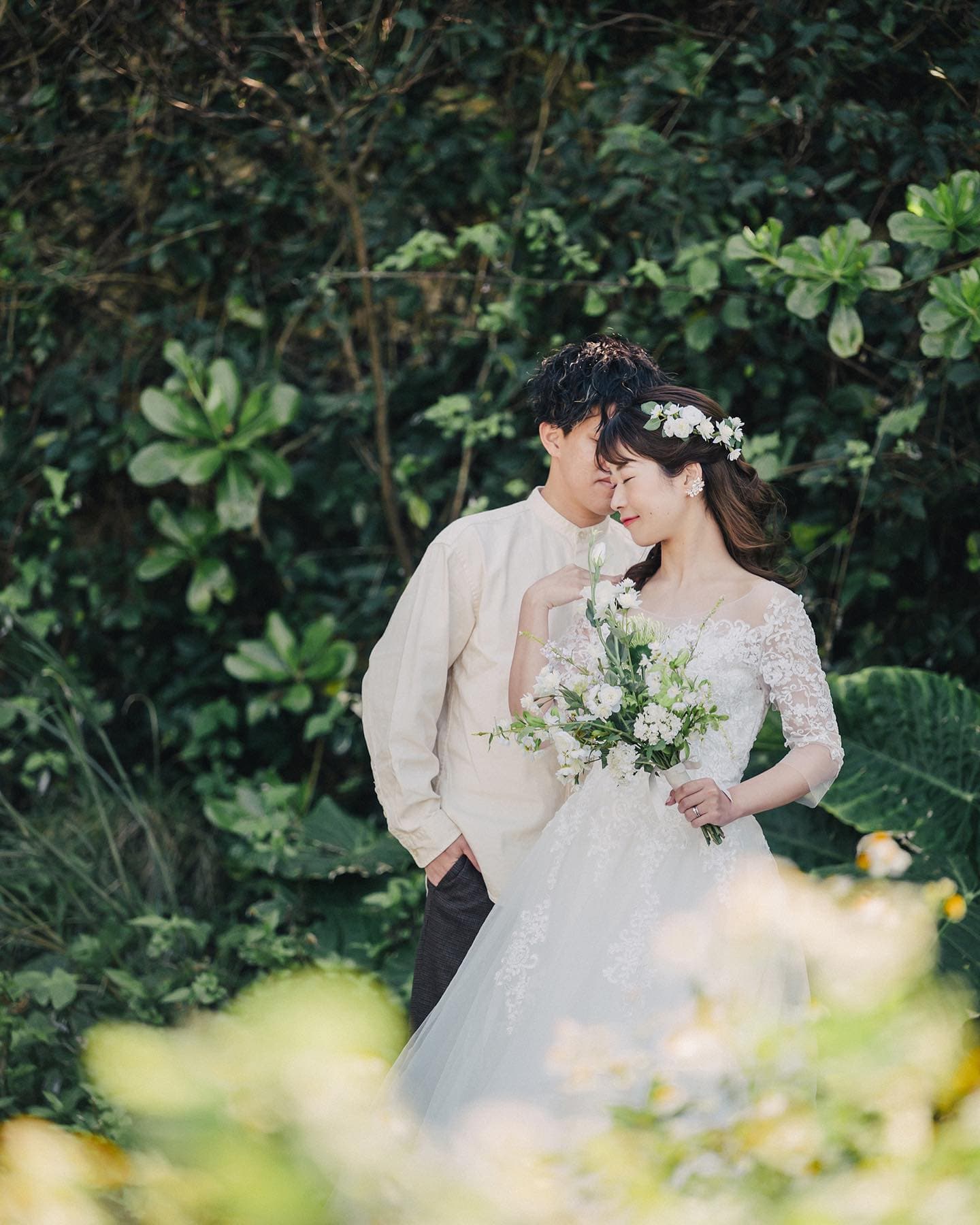 Groom nuzzling close to the bride in a flower crown amid lush Okinawa greenery