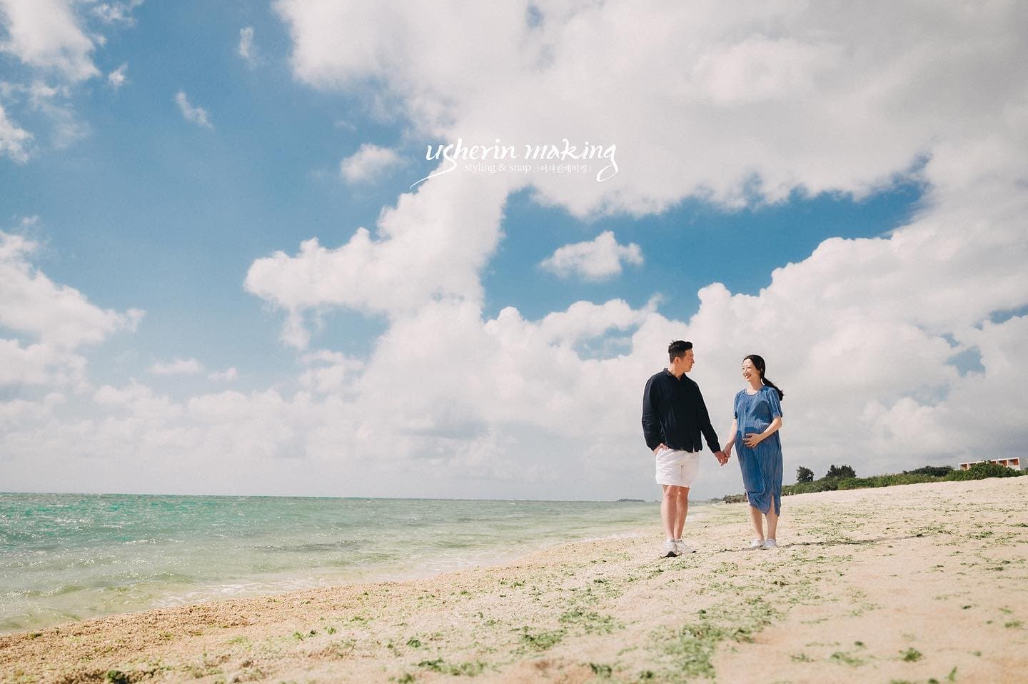Expecting couple walking hand in hand on an Okinawan beach under a blue sky